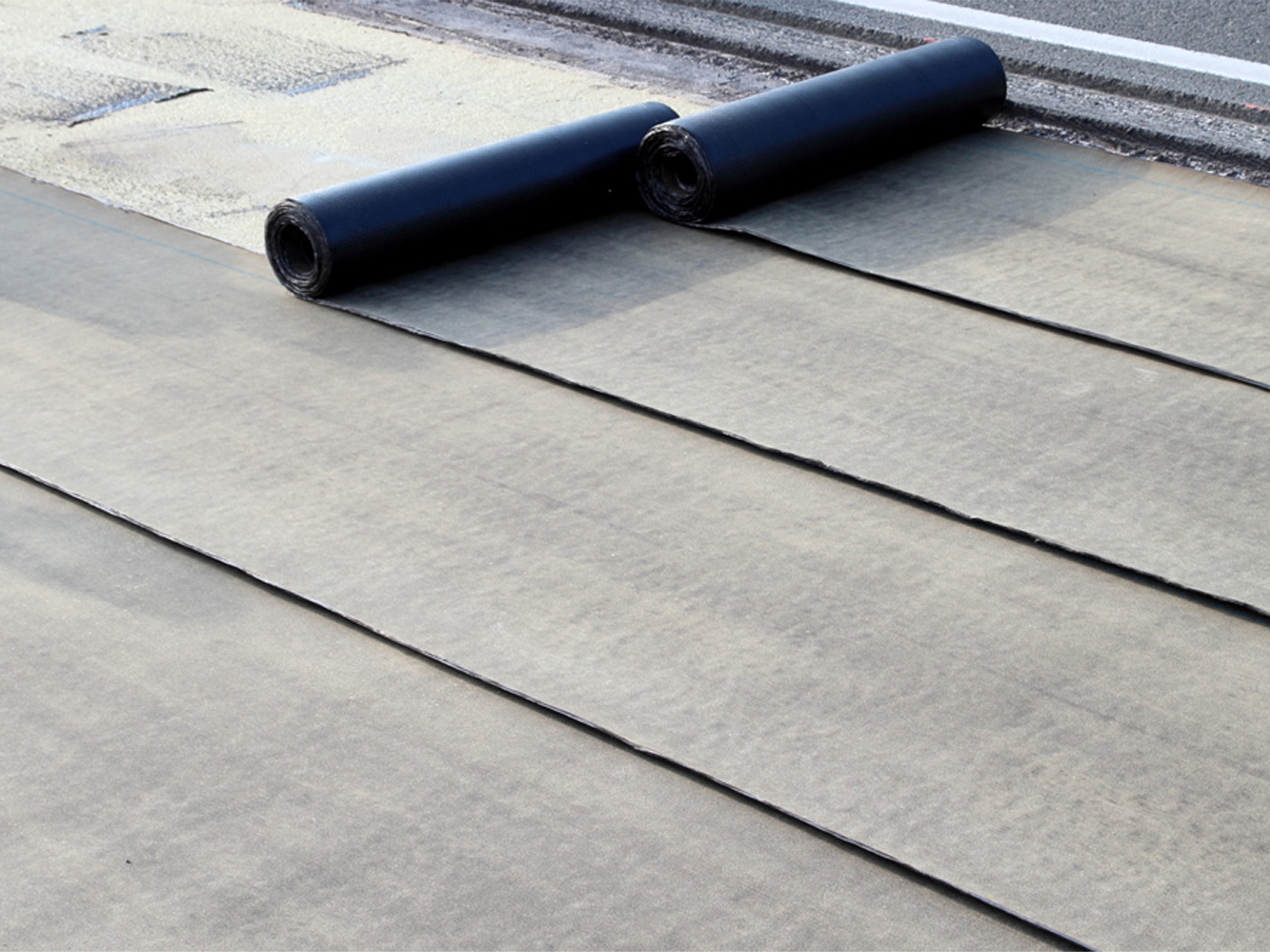 Two rolls of roofing material are laying on a concrete surface.