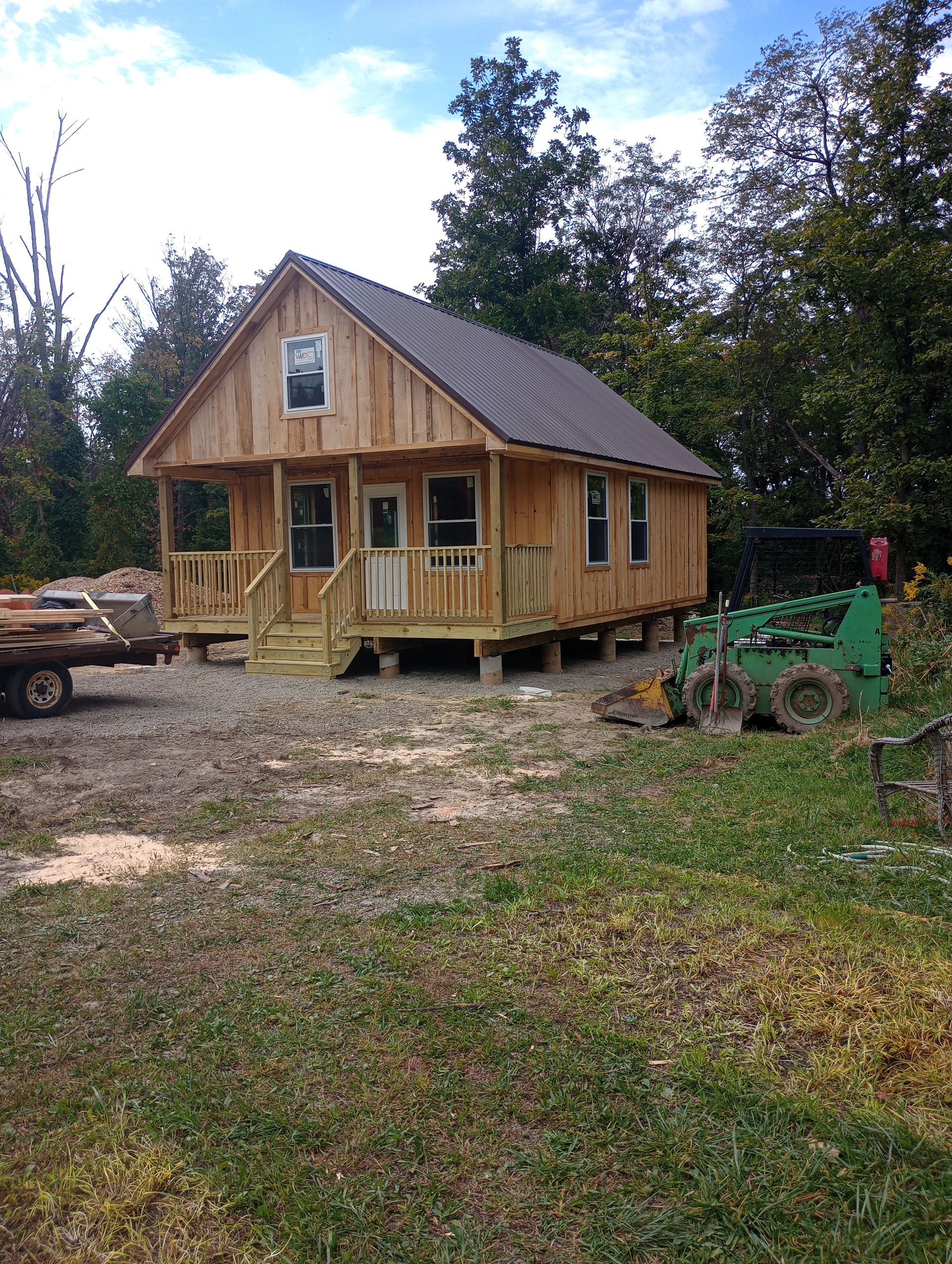 A small wooden house with a porch is sitting in the middle of a grassy field.