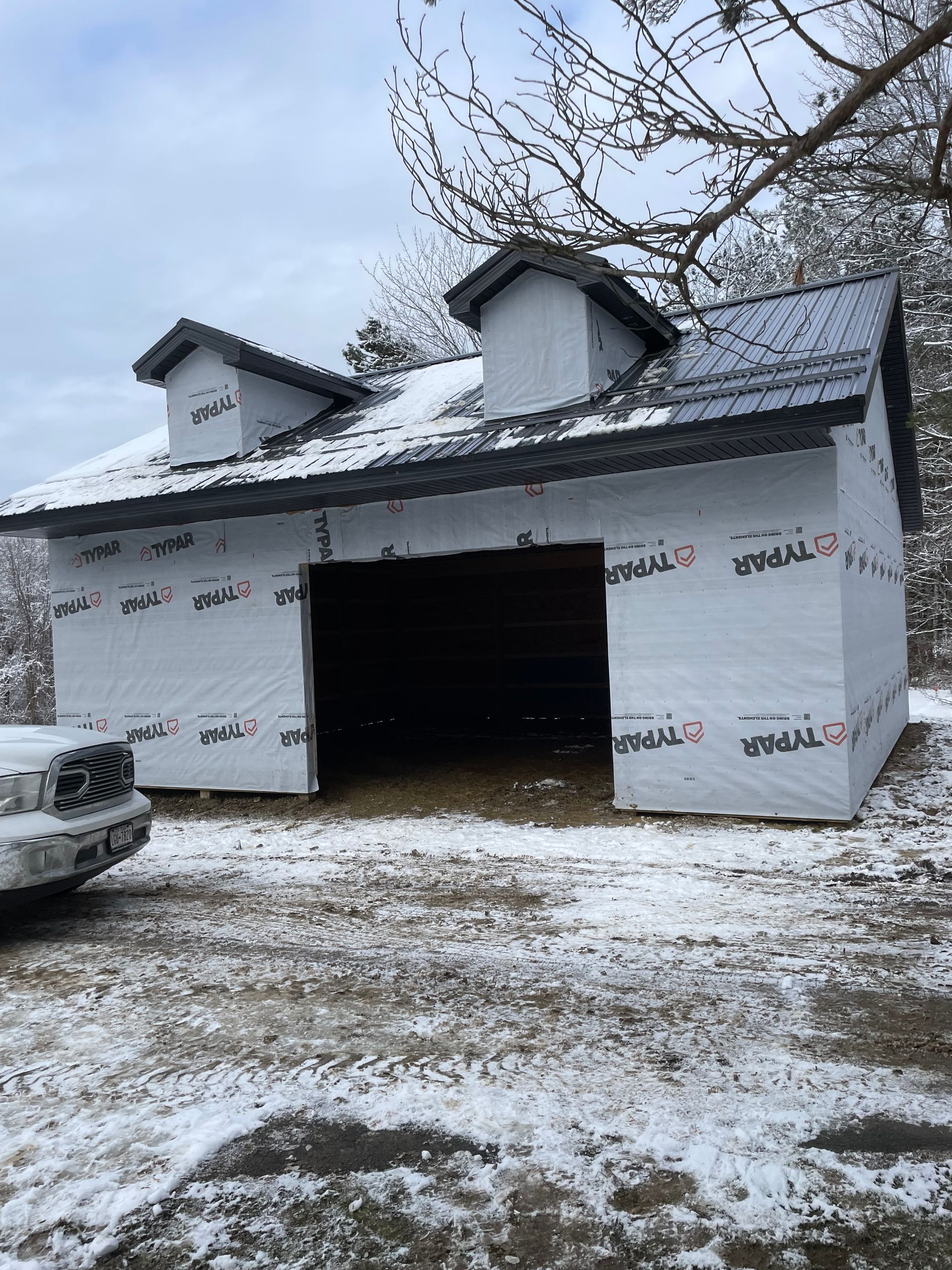 A garage is being built in the snow with a truck parked in front of it.