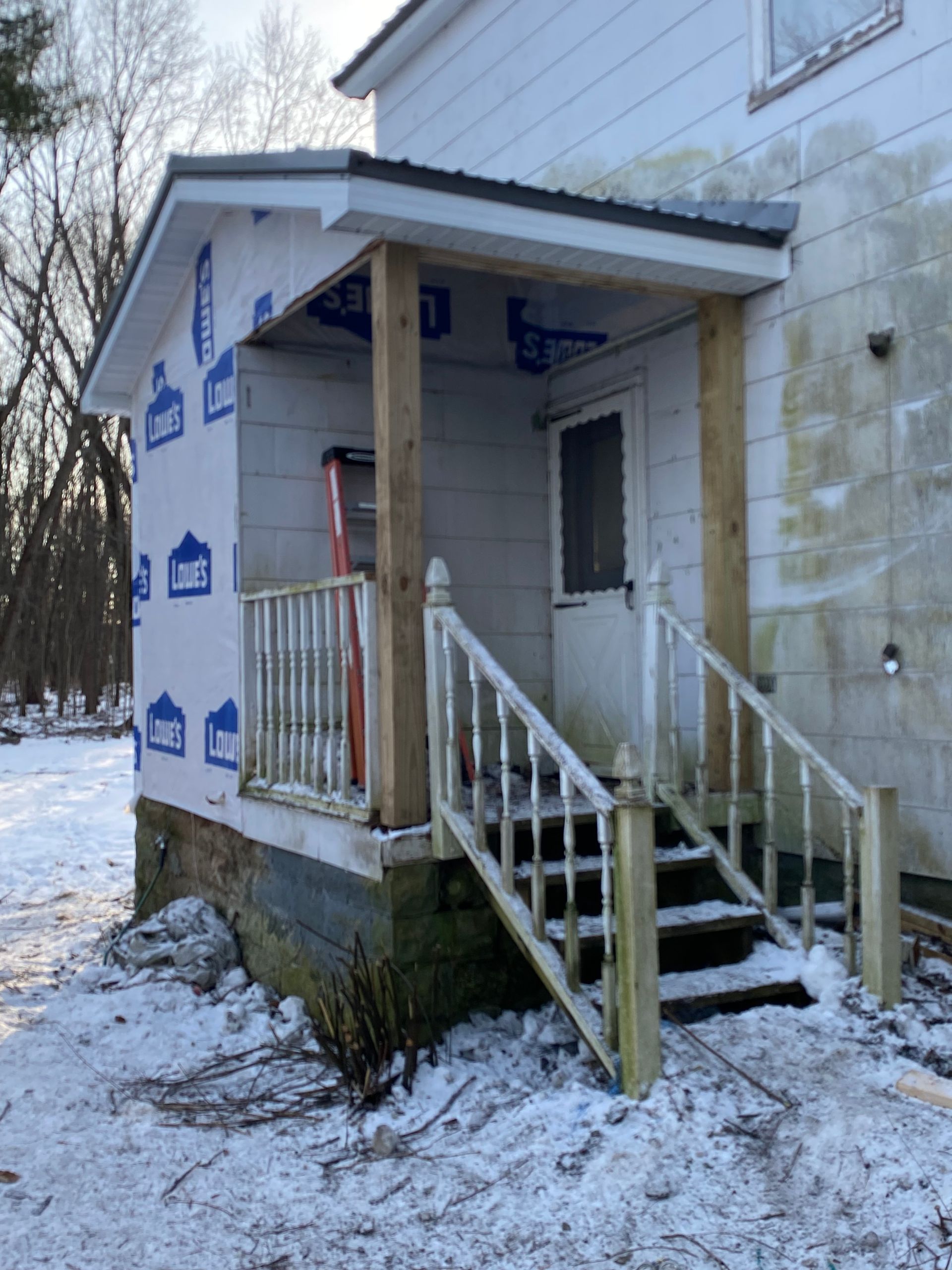 A white house with a porch and stairs in the snow