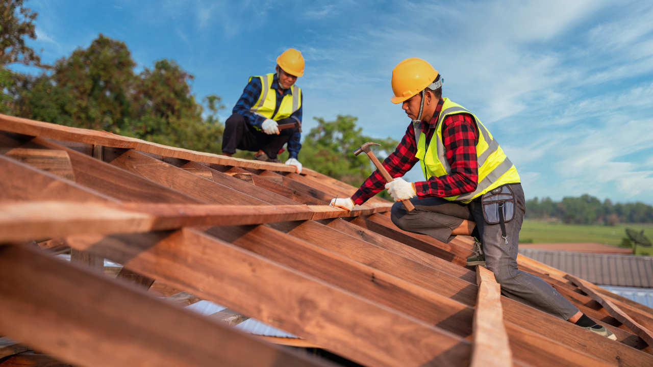 Two construction workers are working on a wooden roof.