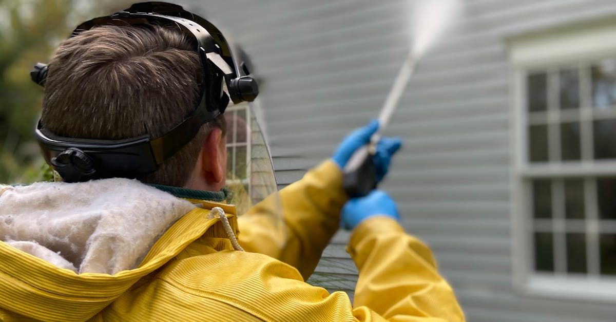 A man in a yellow jacket is cleaning a house with a high pressure washer.