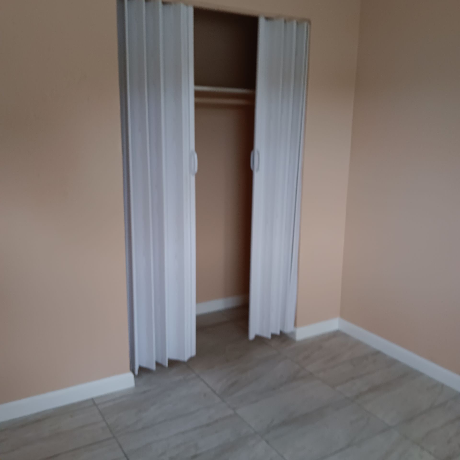 Empty closet with white folding doors in a room with peach walls and tile floor.