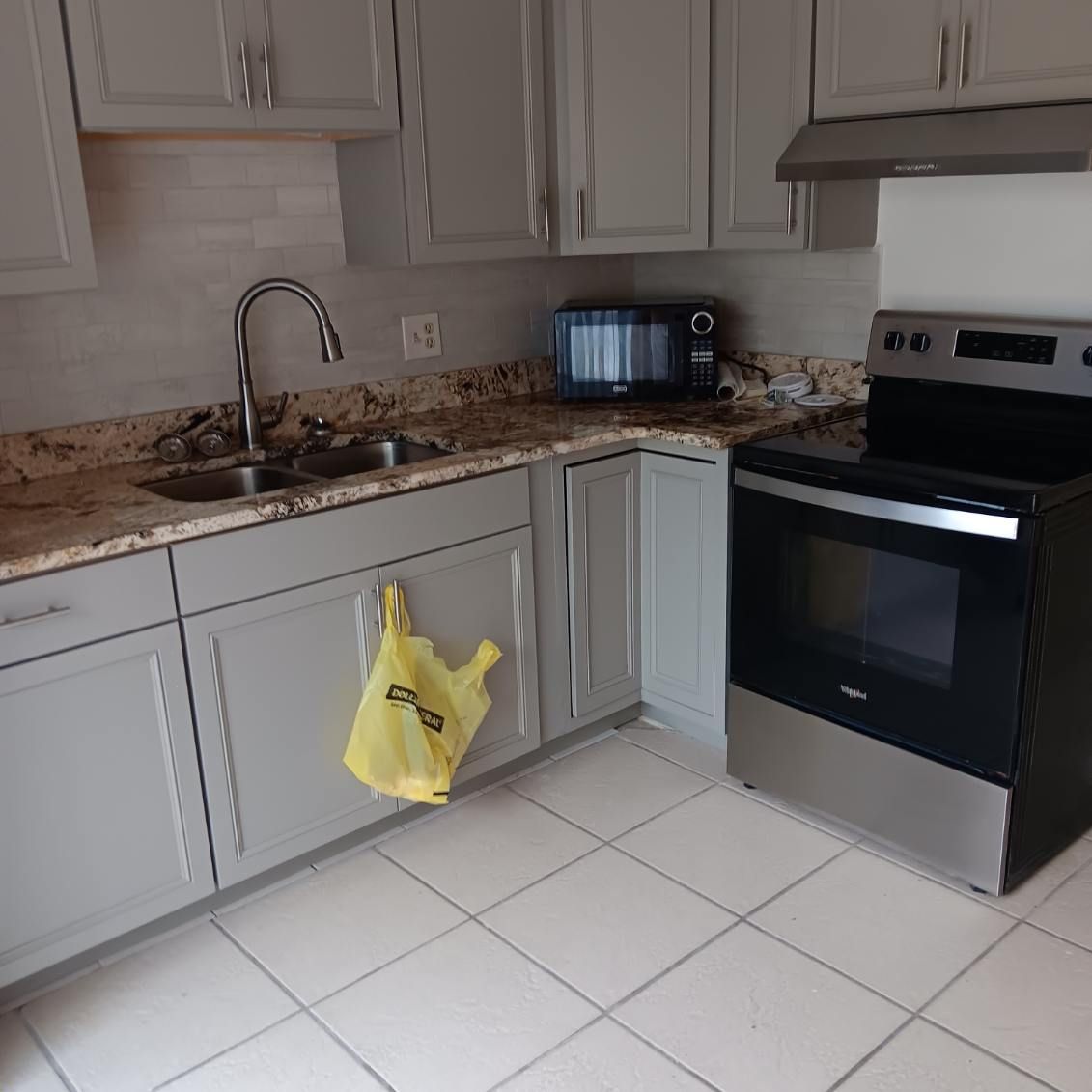 Kitchen with gray cabinets, a silver stove, and a microwave. A yellow bag hangs on a cabinet.
