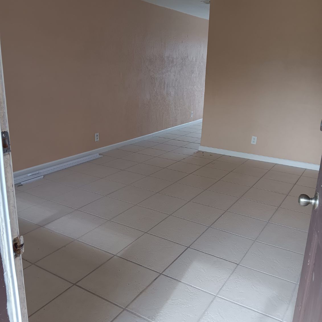 Empty room with beige tiled floor and walls, door frame in view.