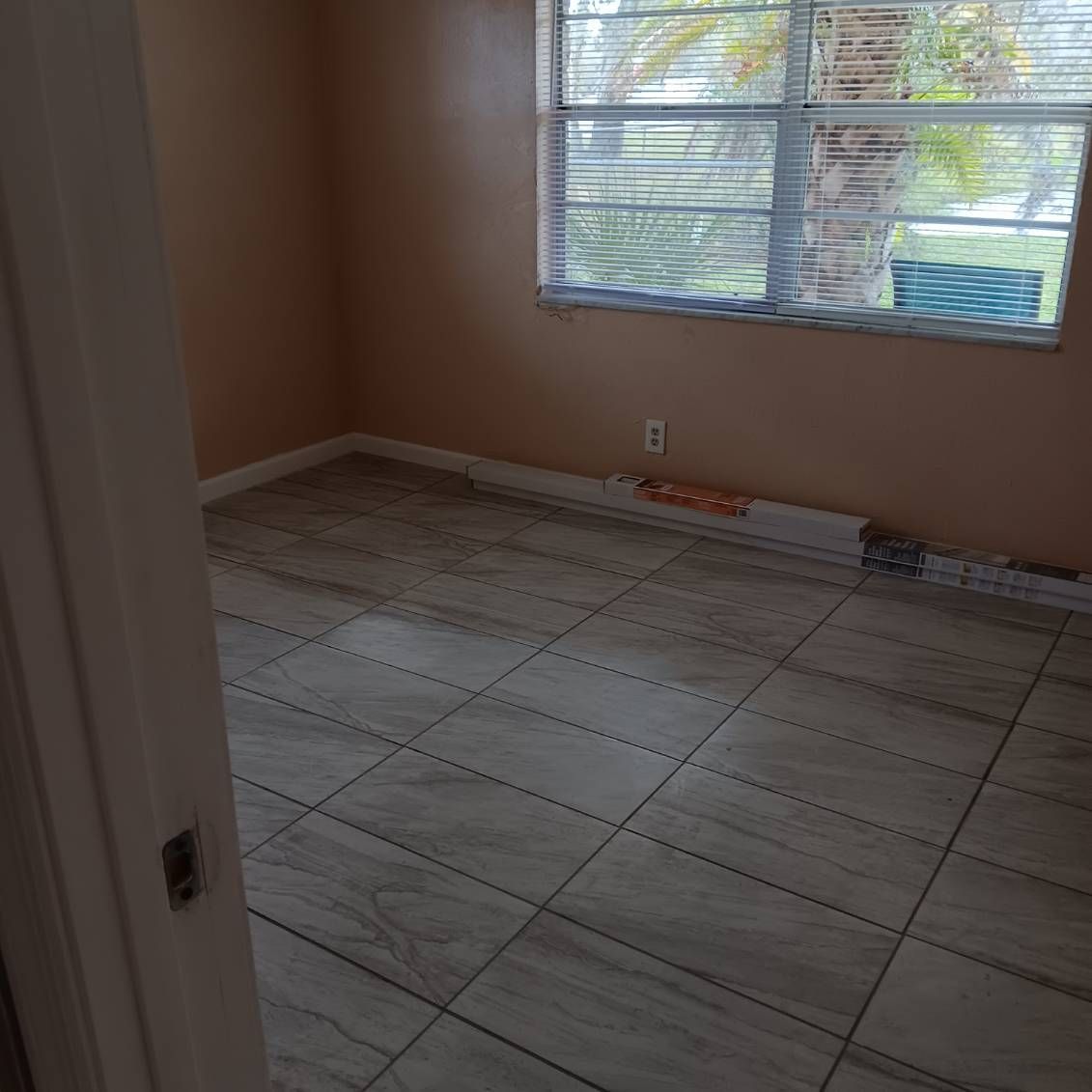 Empty room with tiled floor and window, peach walls, and partial view of door.