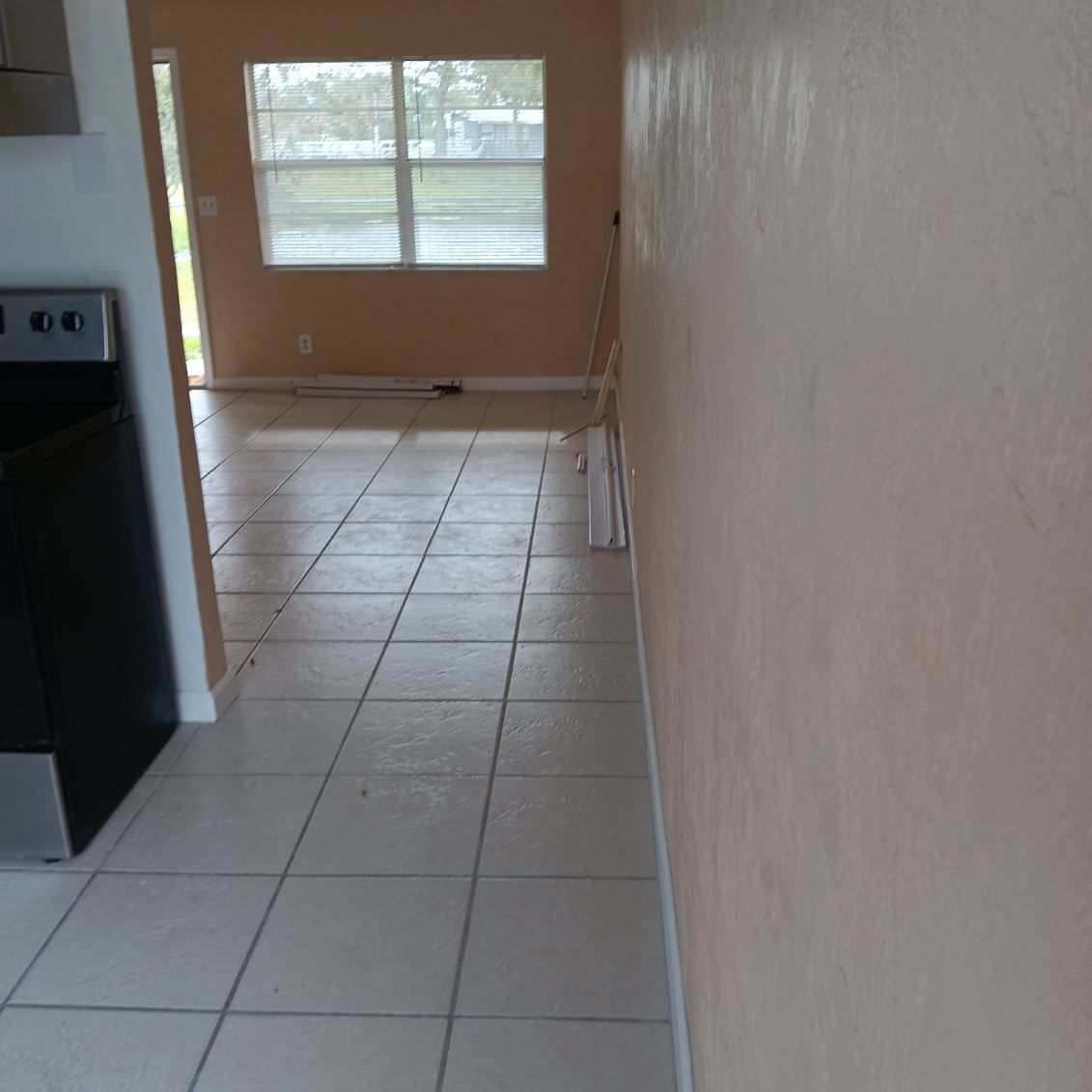 Tiled floor leads to a room with a window; off-white walls, an appliance on the left.