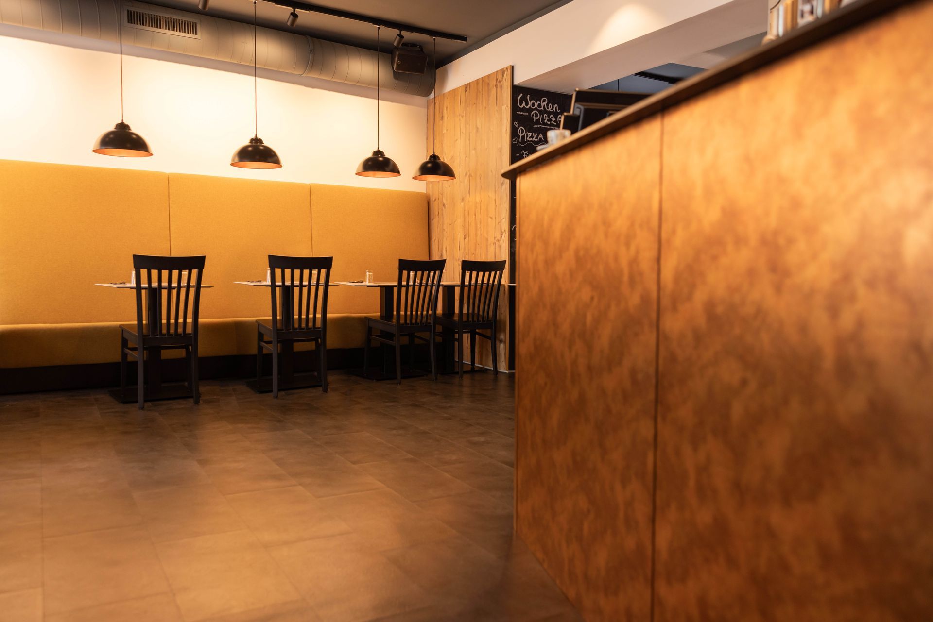Restaurant-Essbereich mit senffarbener Wandverkleidung, Holzstühlen und Pendelleuchten.