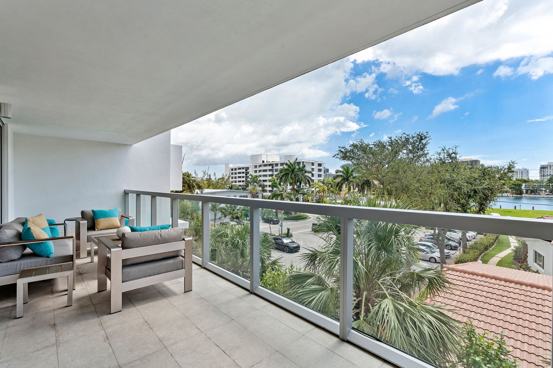 Balcony with outdoor furniture, glass railing, and city view on a sunny day.