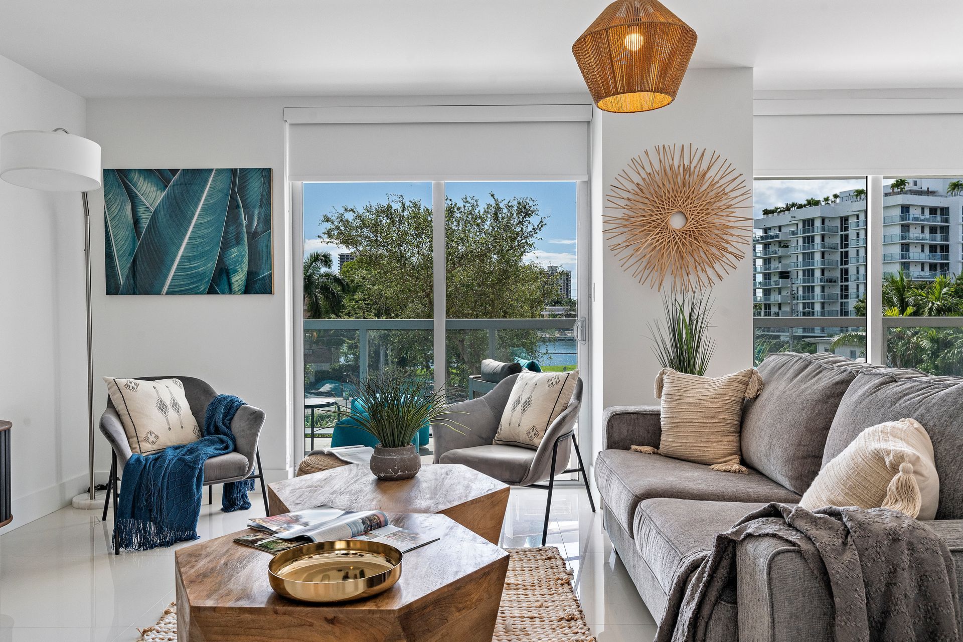 Living room with gray sofa, chairs, wood table, and large windows overlooking a balcony.