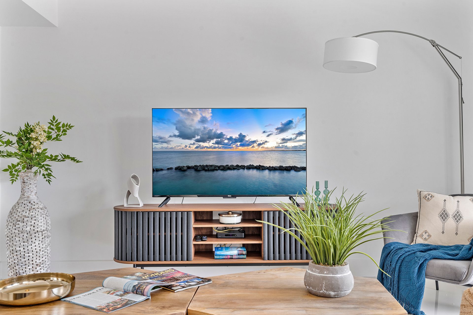 Living room with TV on wooden cabinet, a plant, and a curved lamp.