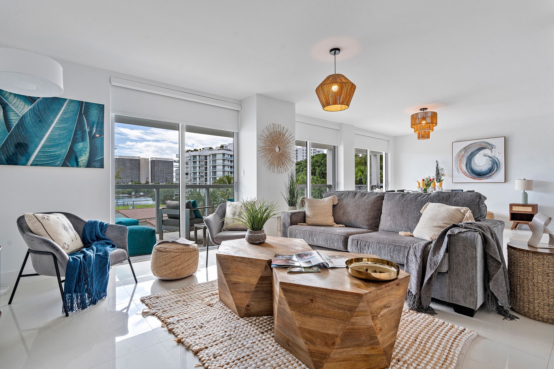 Bright living room with gray sofa, wooden tables, and balcony overlooking a modern cityscape.