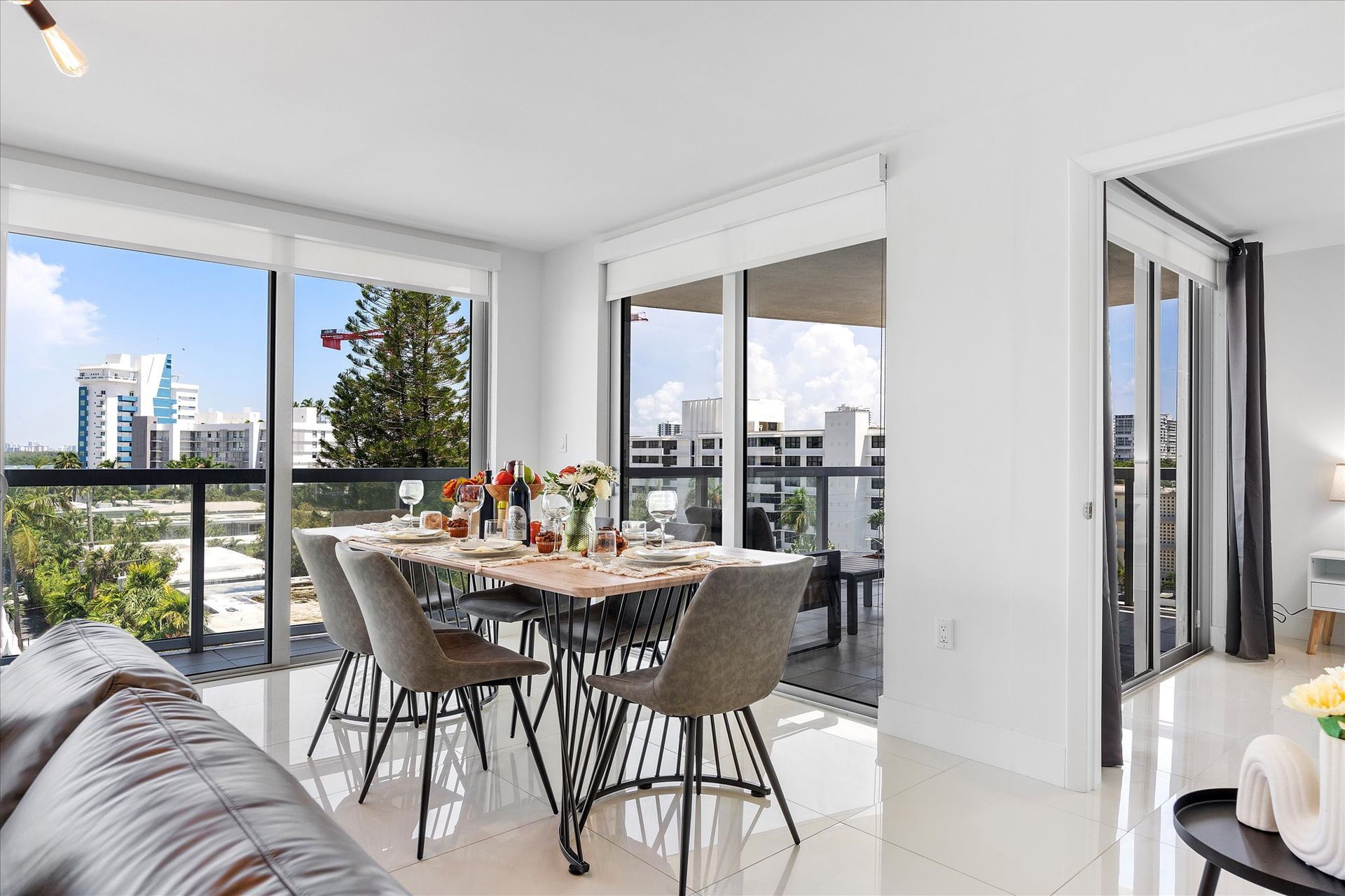 Dining room with a table set for a meal, large windows, and a balcony with a city view.