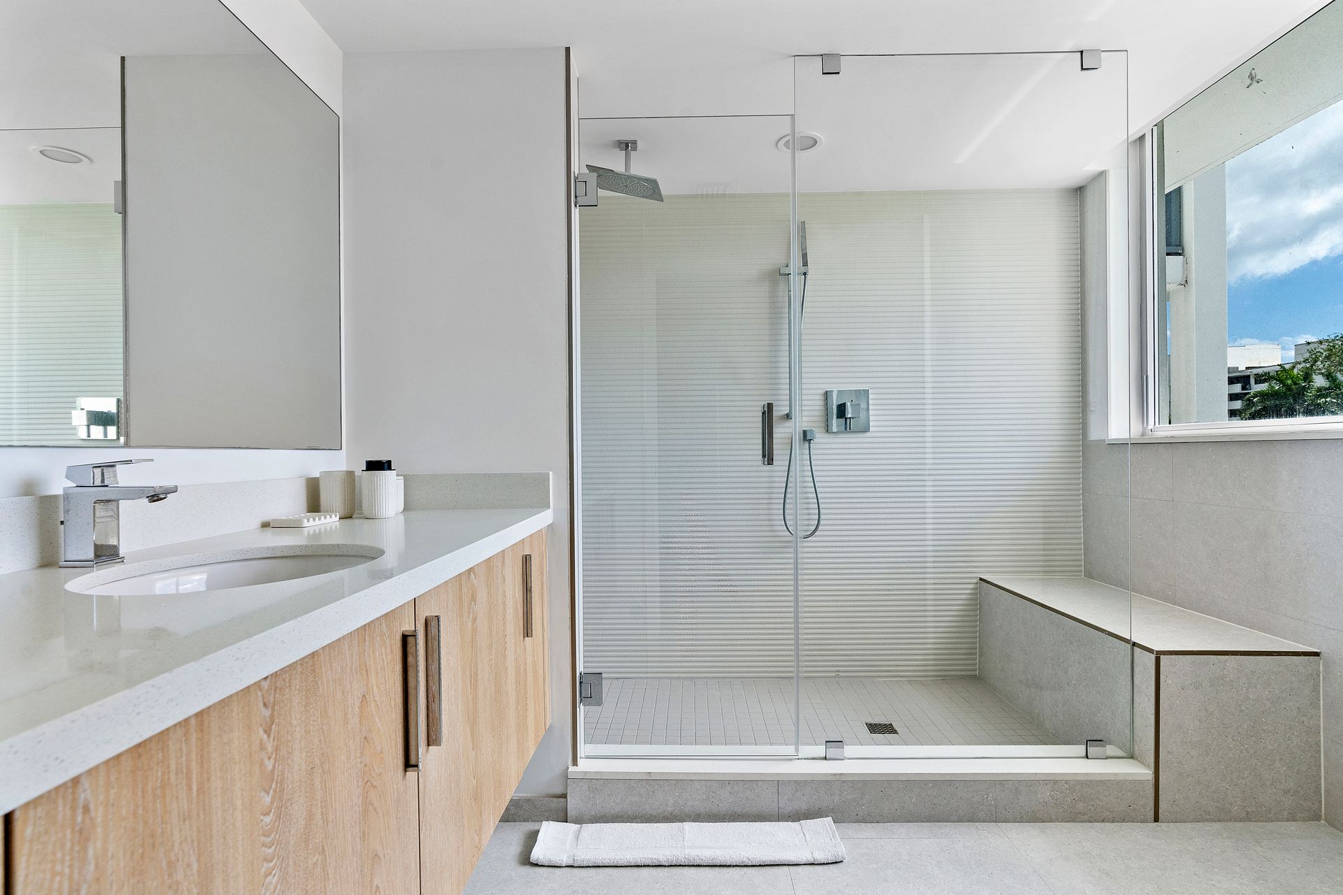 Modern, light-filled bathroom with a glass-doored shower, vanity with wooden cabinets, and a window.