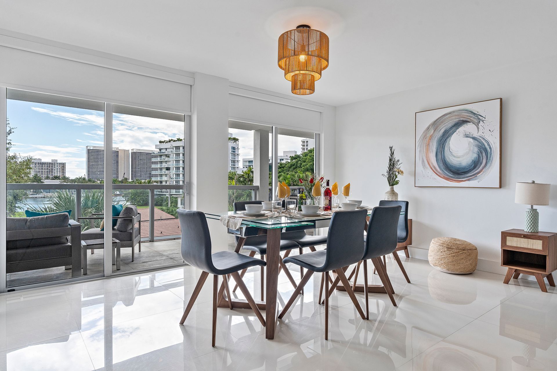 Dining room with table, chairs, and balcony with city view. White walls, glossy floor.