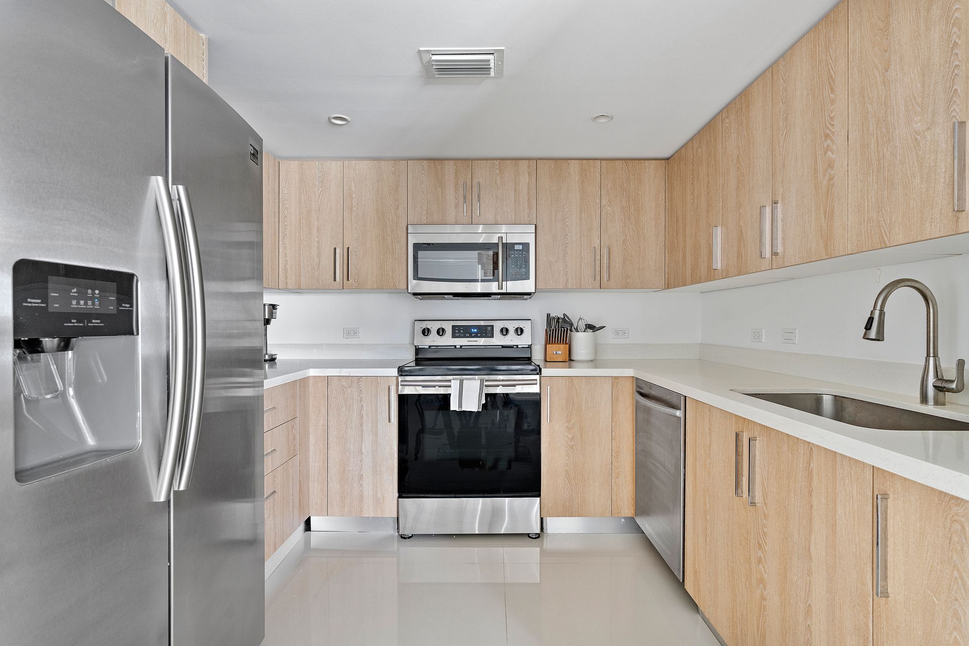 Modern kitchen with light wood cabinets, stainless steel appliances, and white countertops.