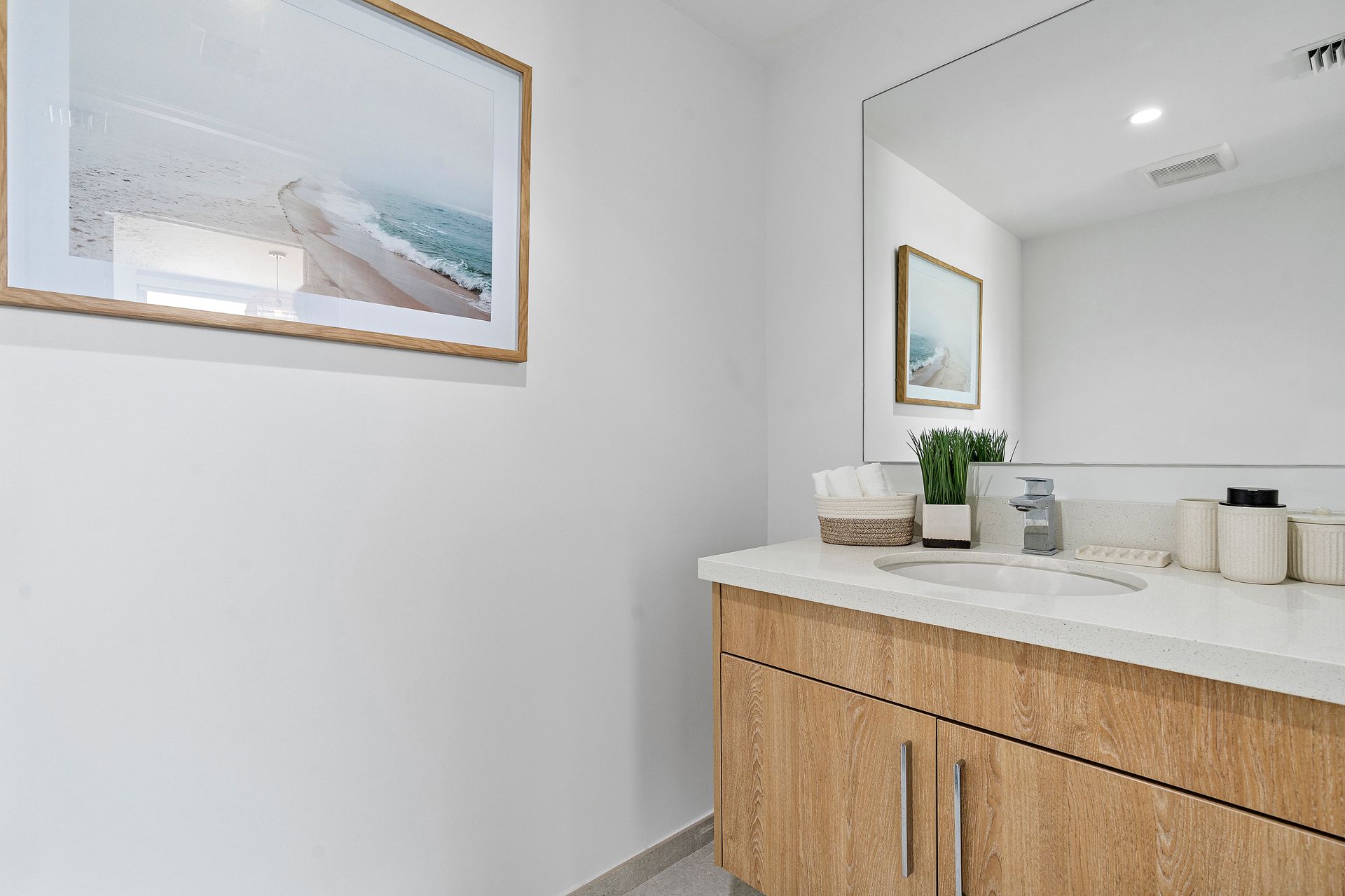 Bathroom with a wood vanity, white countertop, and a mirror with a framed coastal art print.