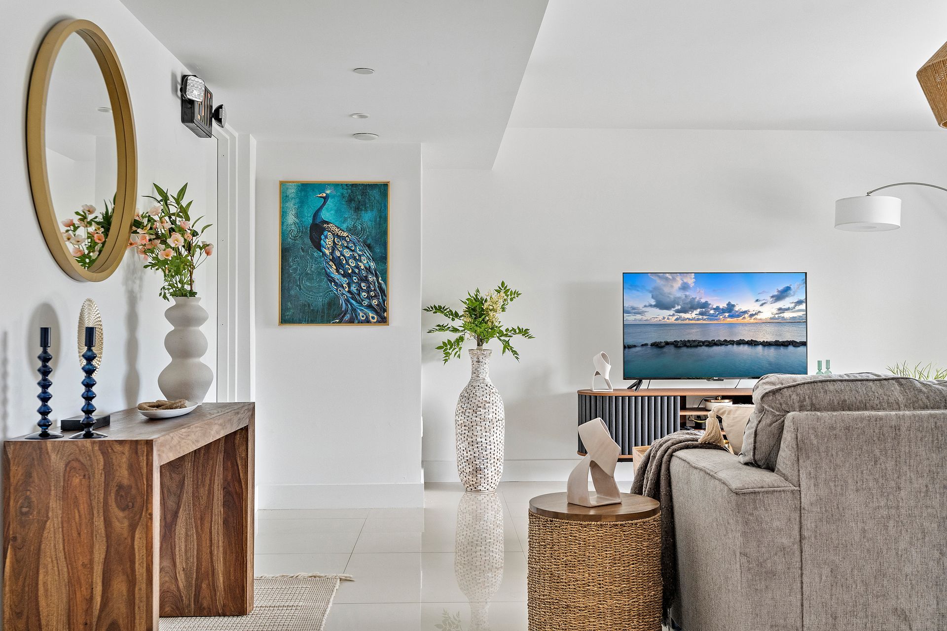 Living room with white walls, wooden console table, peacock art, TV, and gray sofa.