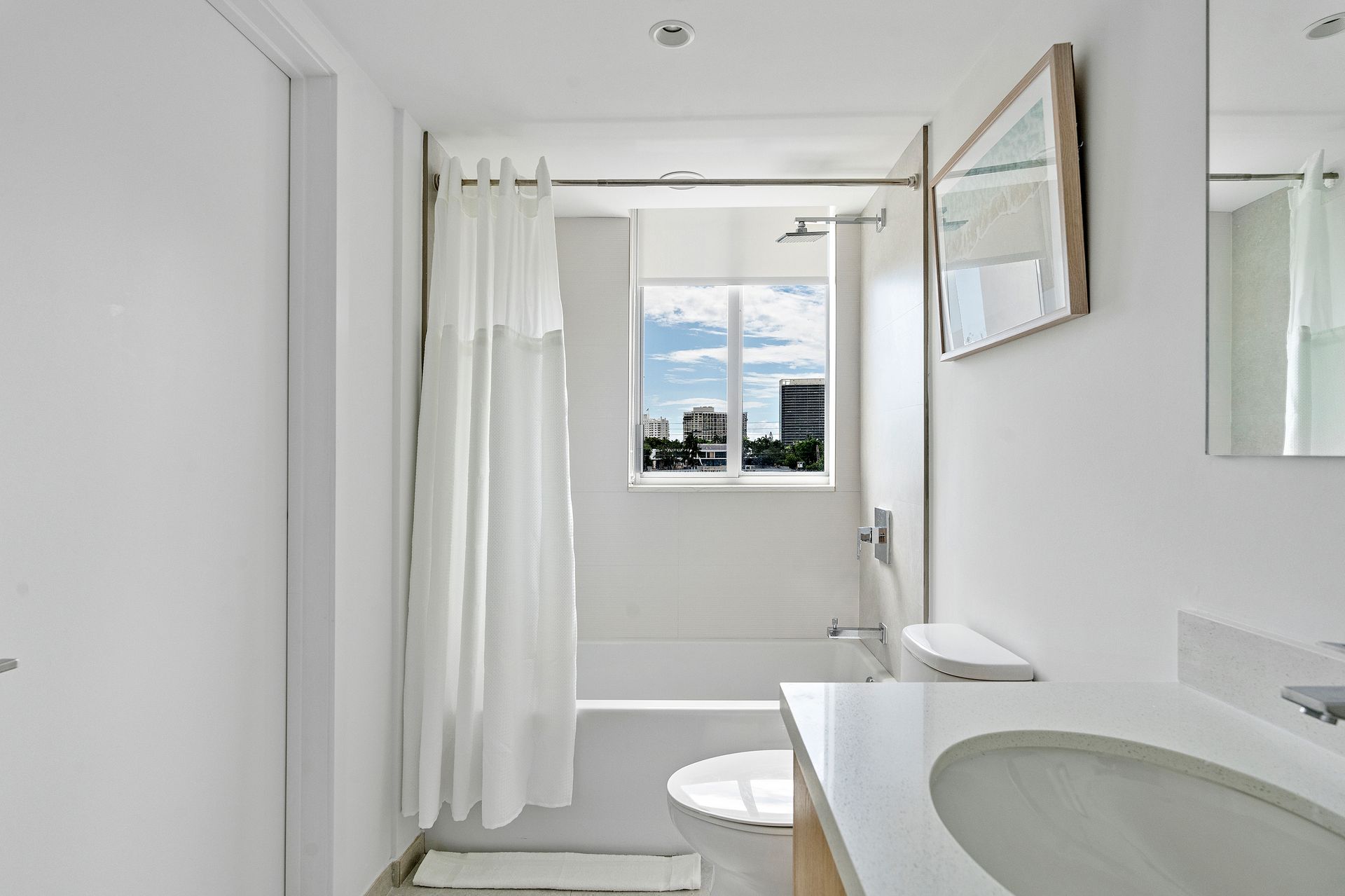 White bathroom with a window, shower, toilet, and sink.