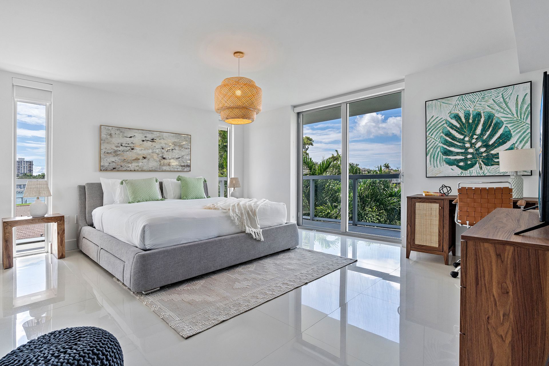 Bright bedroom with gray bed, white walls, and large windows overlooking trees.