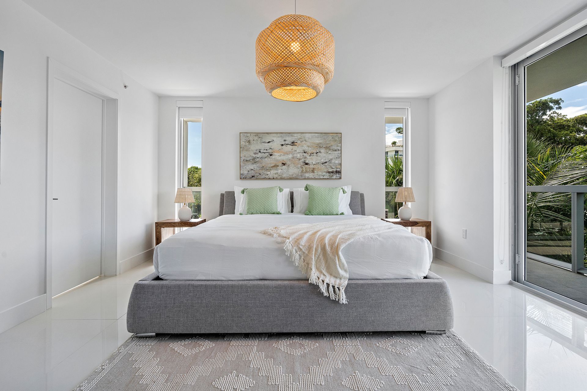 Bedroom with gray bed, woven light fixture, white walls, and balcony.