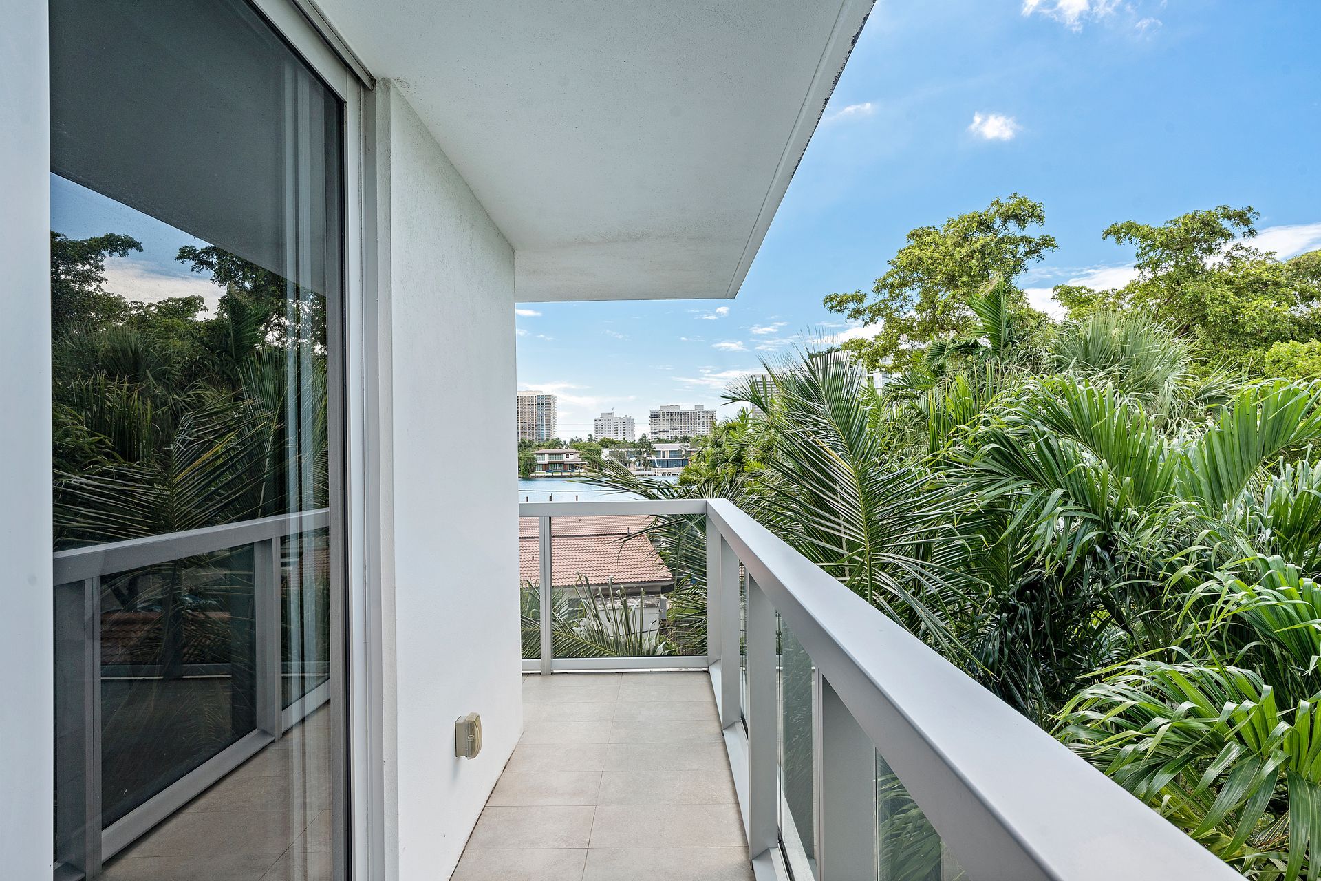 Balcony with white railing overlooking lush green trees and a bright blue sky.