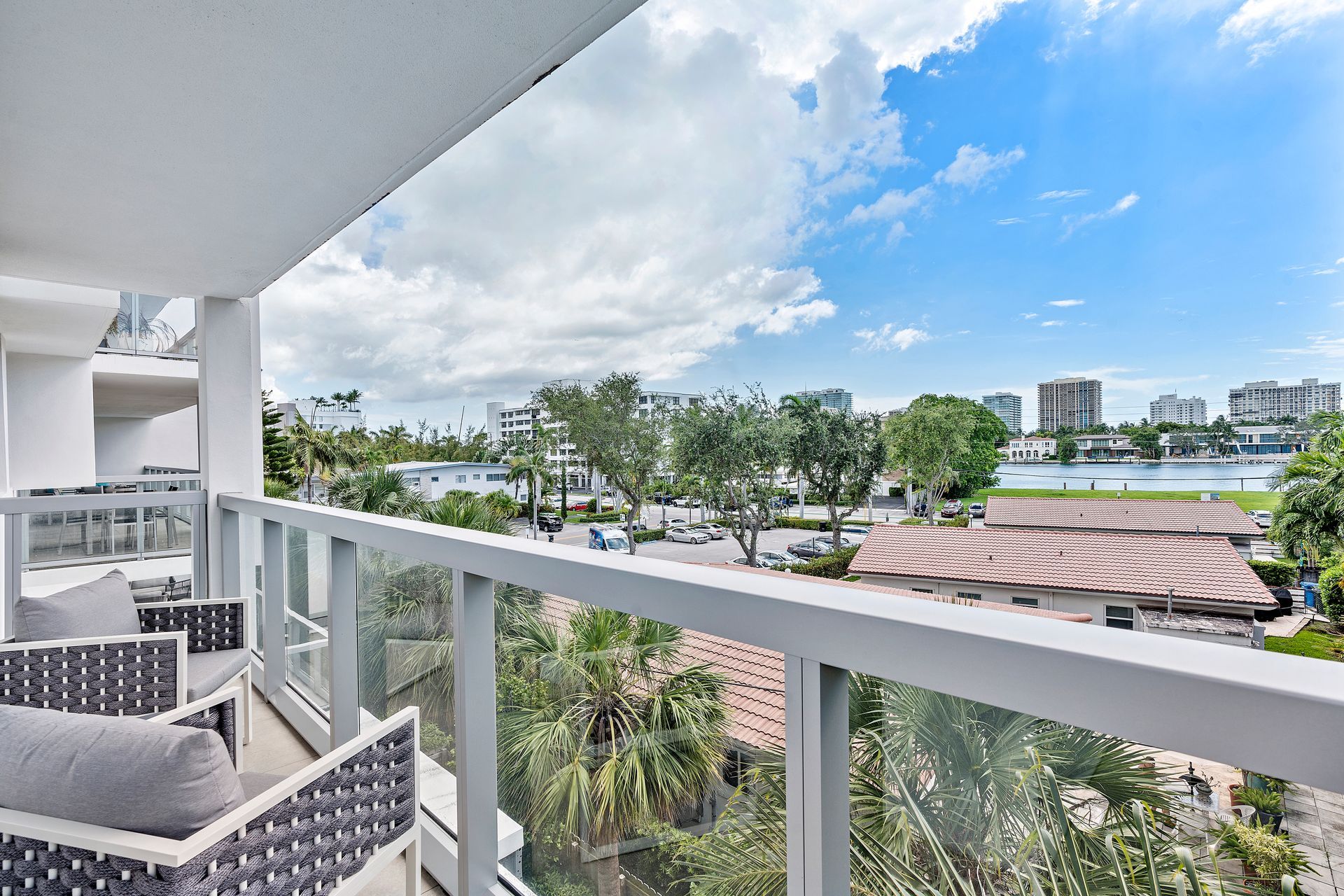 Balcony with seating overlooking a city, water, and sky with clouds.