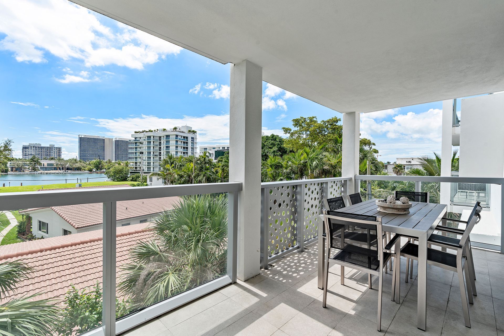 Balcony with table and chairs overlooking buildings and water on a sunny day.