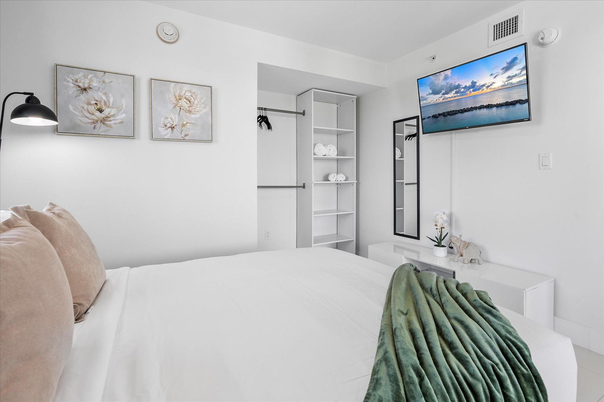 Bright white bedroom with bed, TV, closet, and decorative accents.