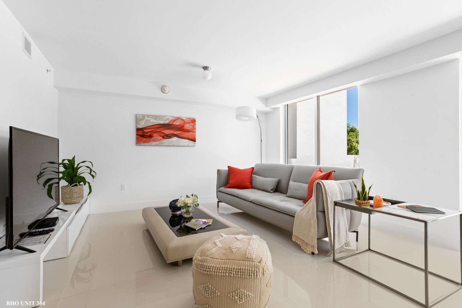 Modern living room with gray sofa, art, and large windows; bright and minimalist.