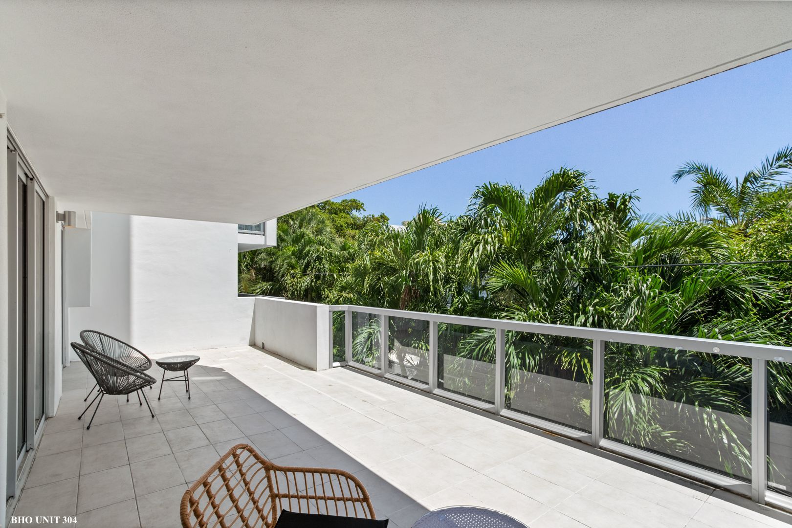 Balcony with chairs overlooking lush green trees and a blue sky.