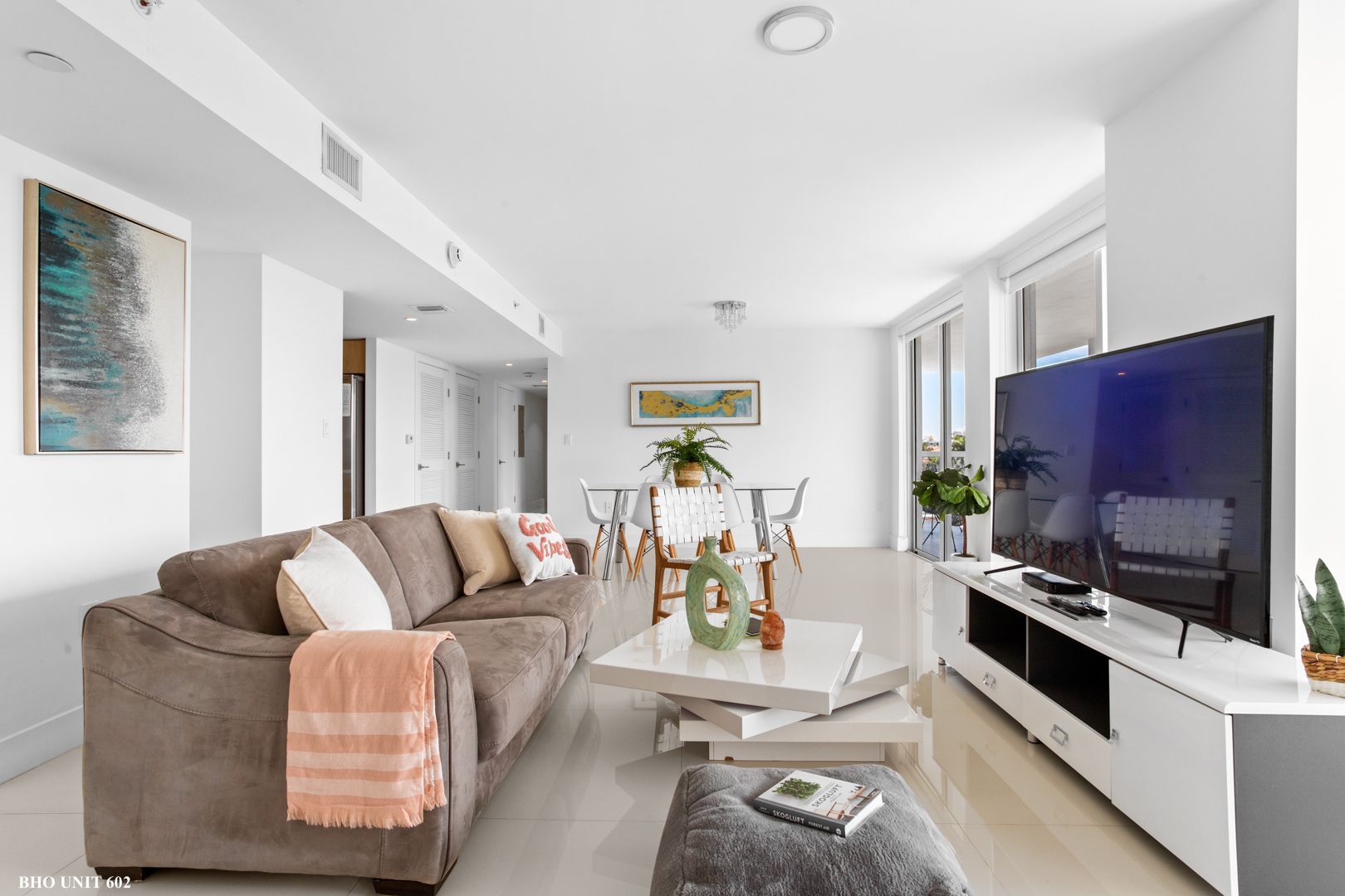 Bright, modern living room with a gray couch, TV, and dining area.
