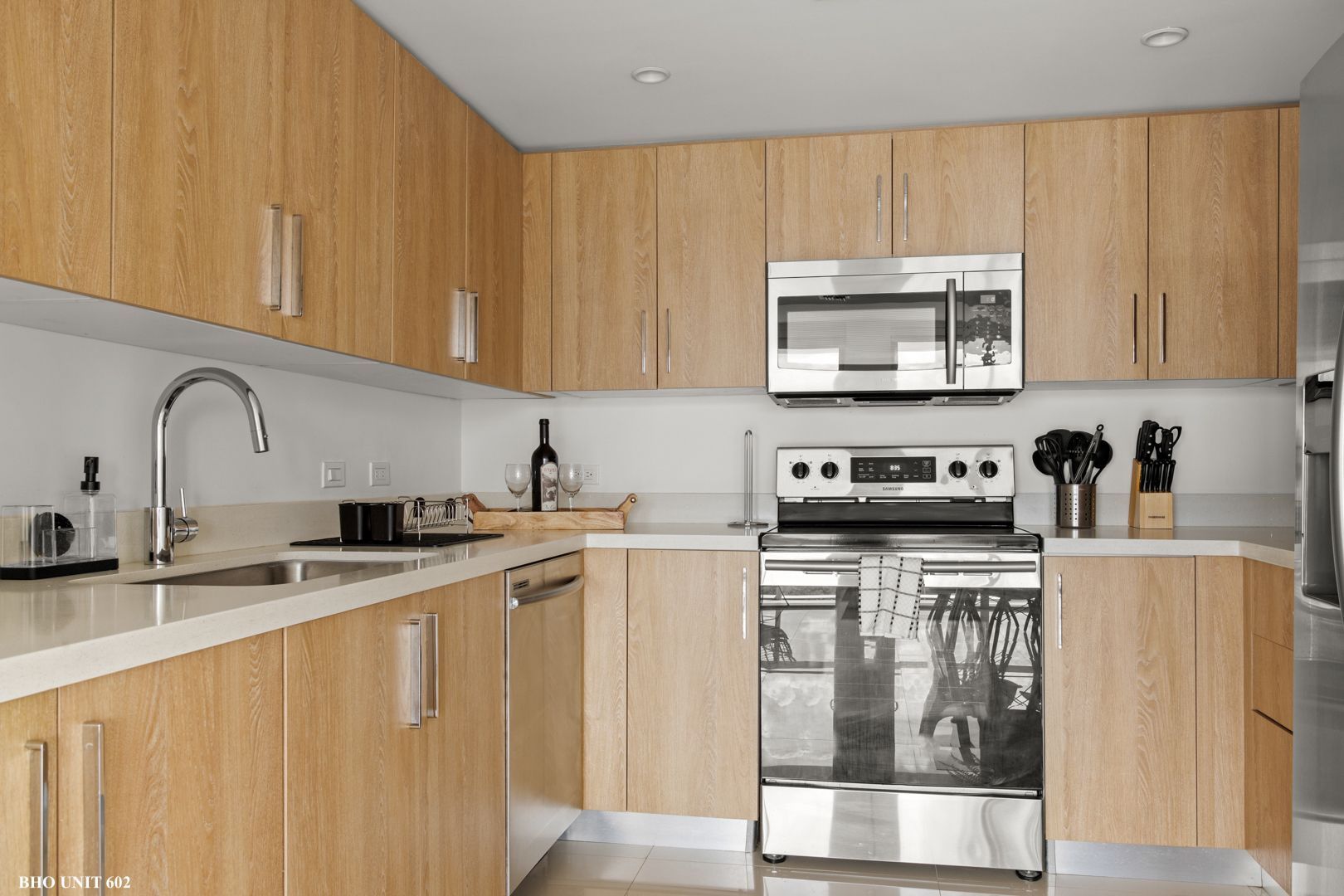 Modern kitchen with light wood cabinets, stainless steel appliances, and white countertops.