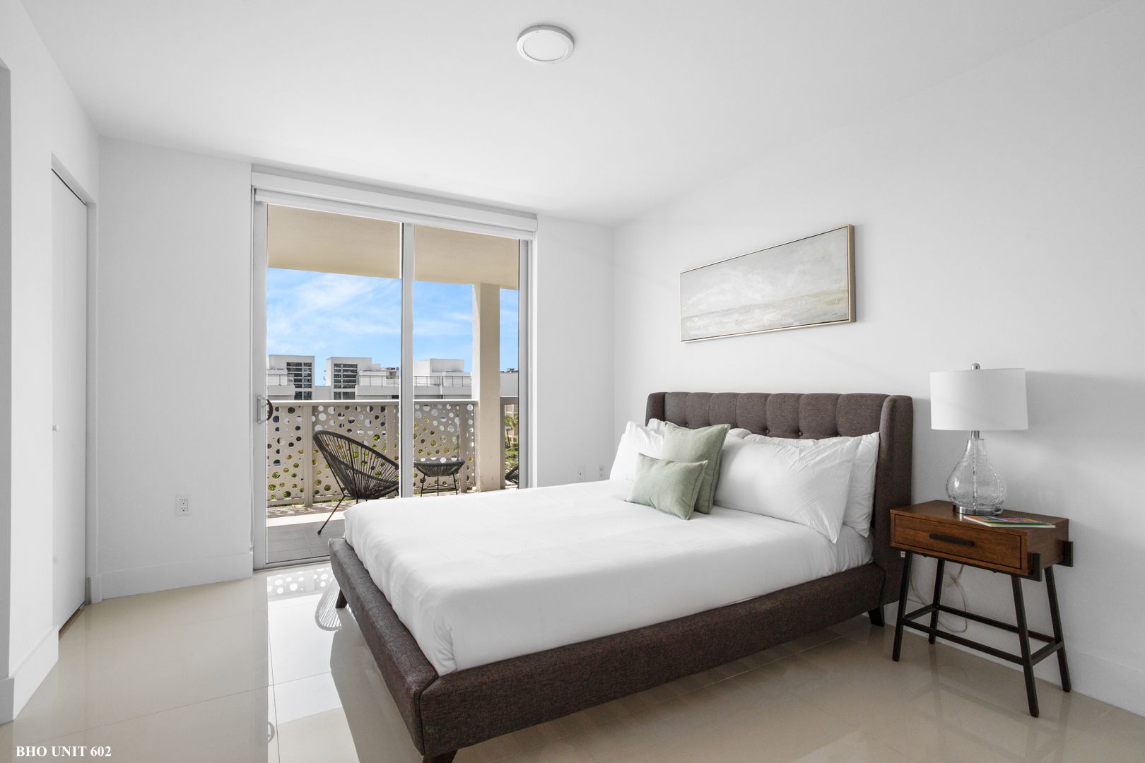 Bedroom with a bed, balcony, and nightstand. Neutral tones, natural light.