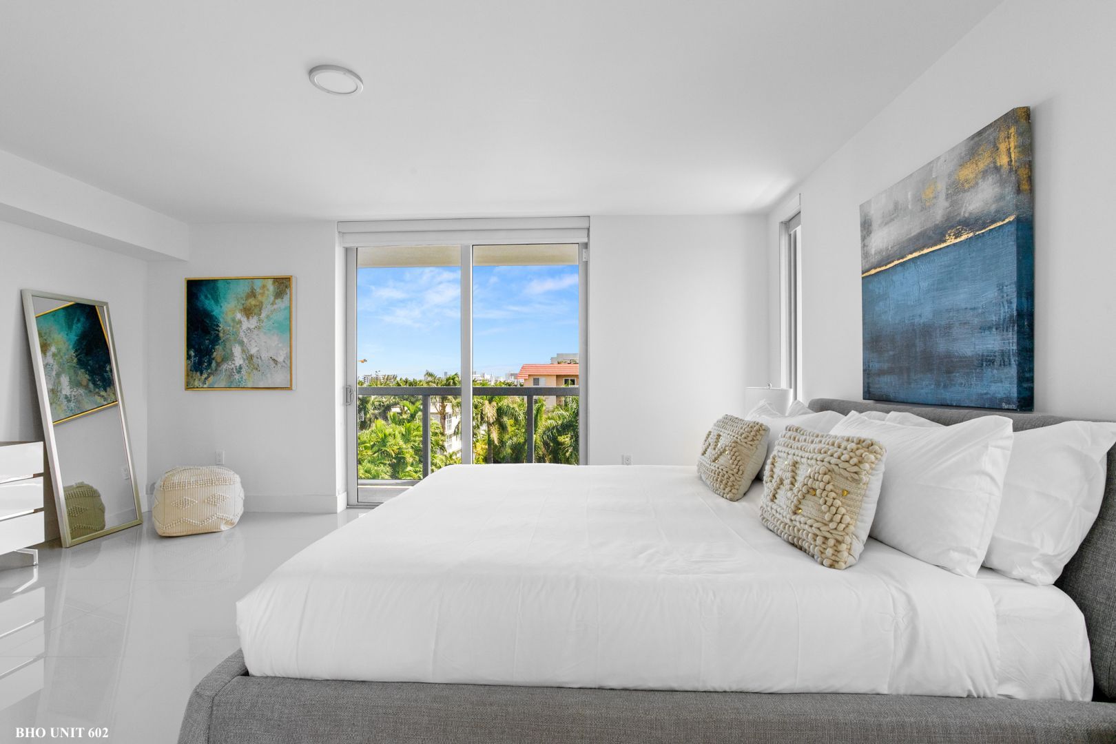 Bright bedroom with a large bed, artwork, and a view of trees through a sliding glass door.