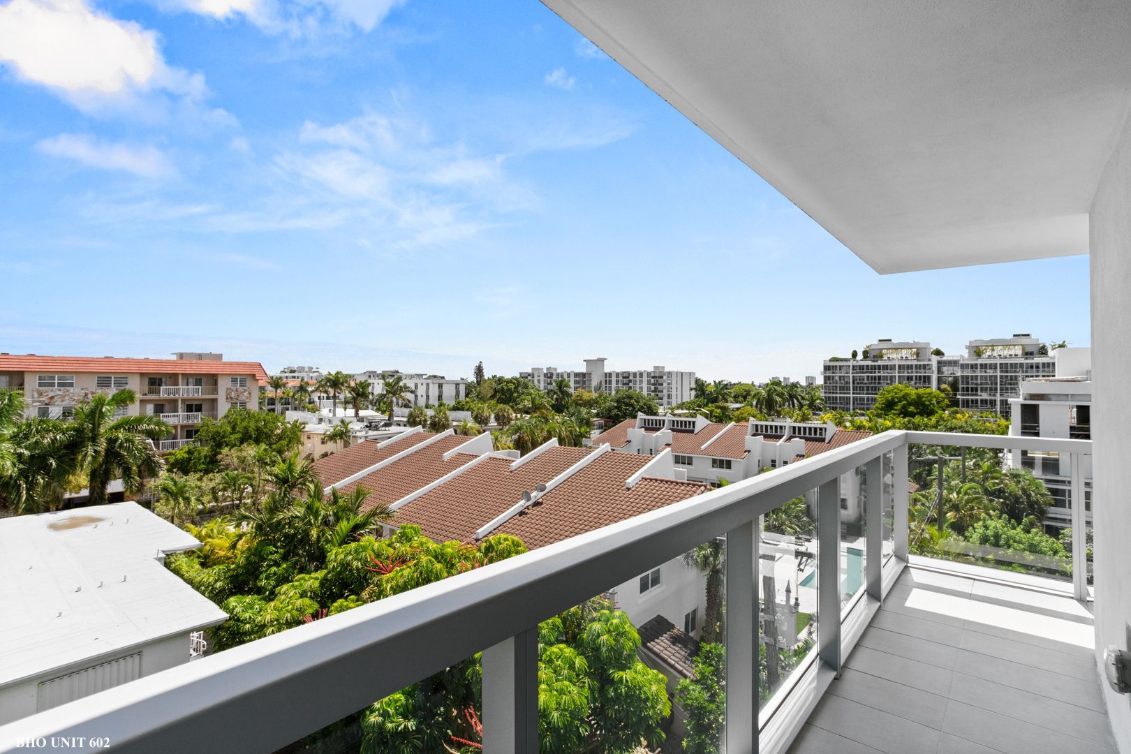 Balcony view overlooking buildings and trees under a blue sky.
