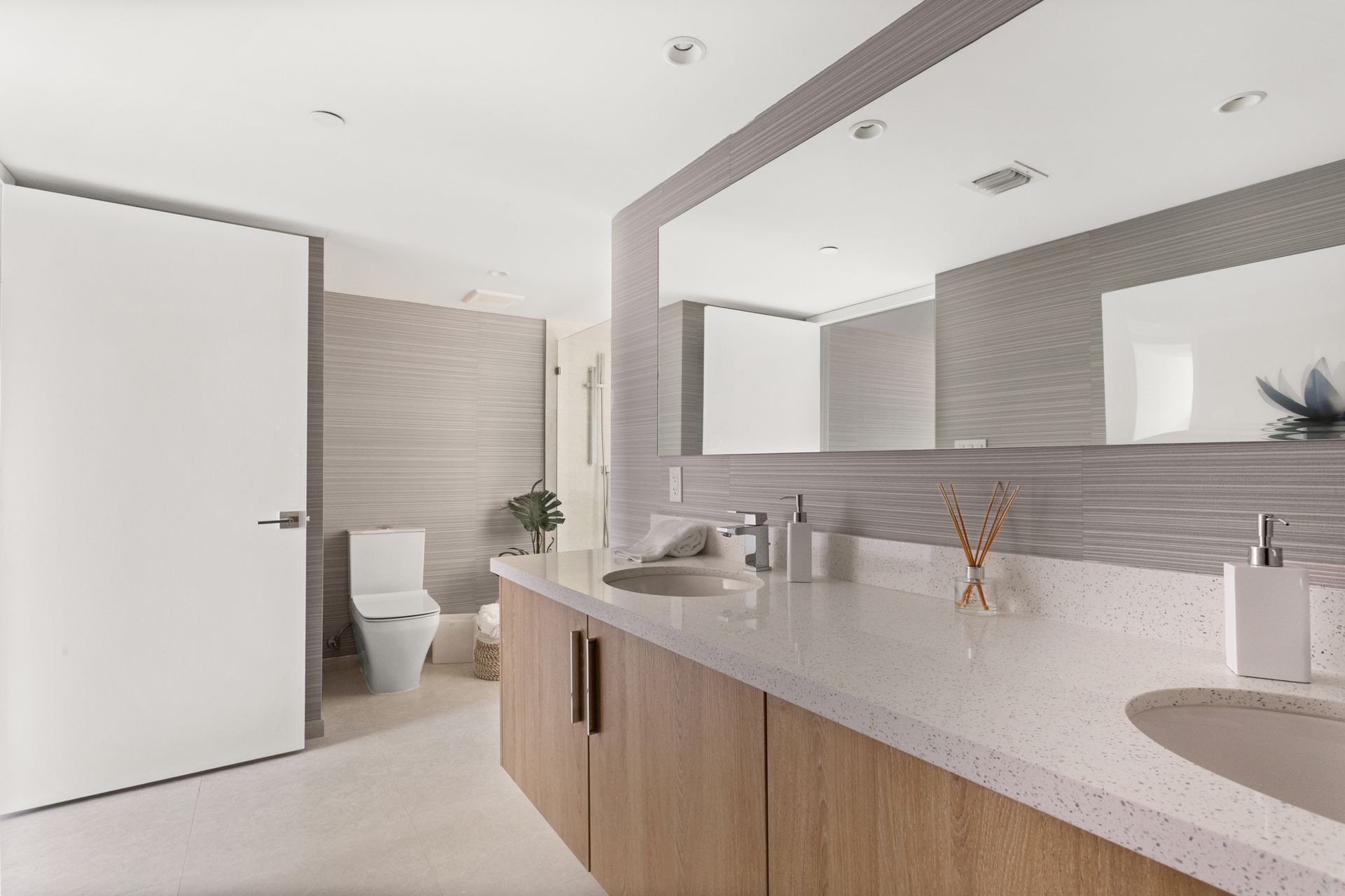 Modern bathroom with double vanity, large mirror, and toilet; light wood cabinets, light-colored countertop, neutral tones.
