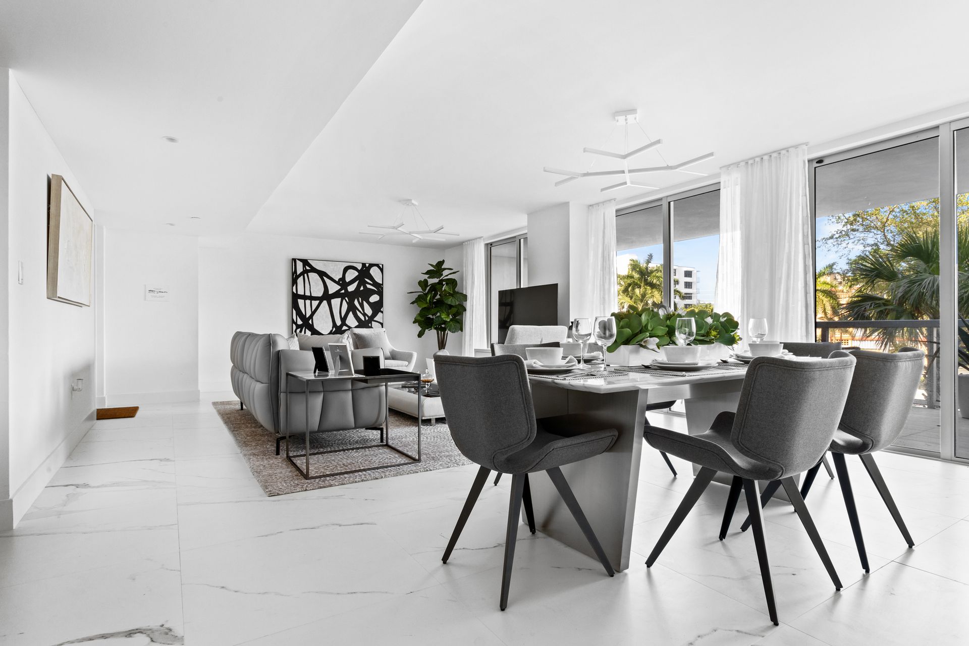 Modern open-plan living and dining area in white with gray furniture and a table set for a meal.