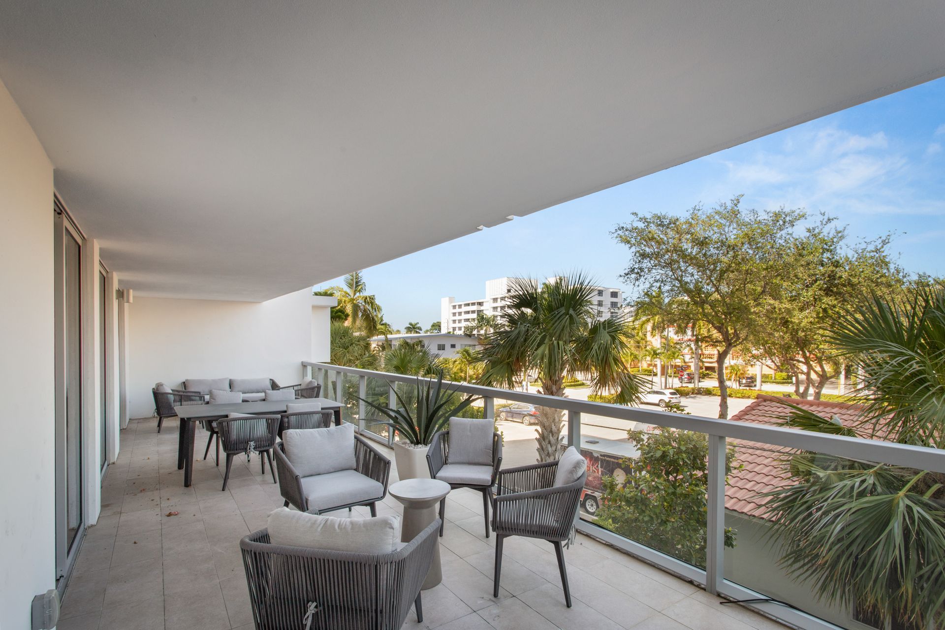 Balcony with outdoor seating overlooking a street with palm trees and buildings.