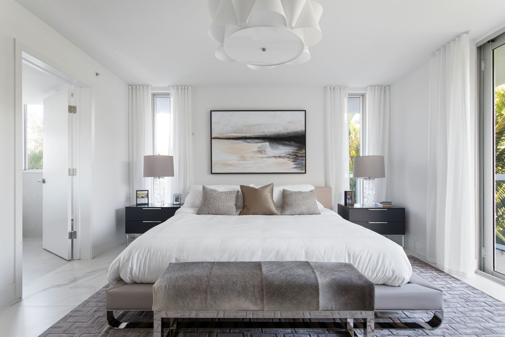 Bright bedroom with white walls, a bed, artwork, and large windows.
