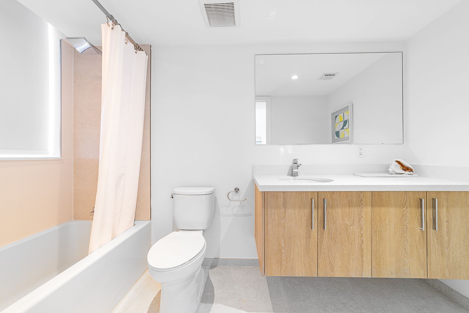 Bright bathroom with white walls, light wood vanity, toilet, and bathtub with shower curtain.