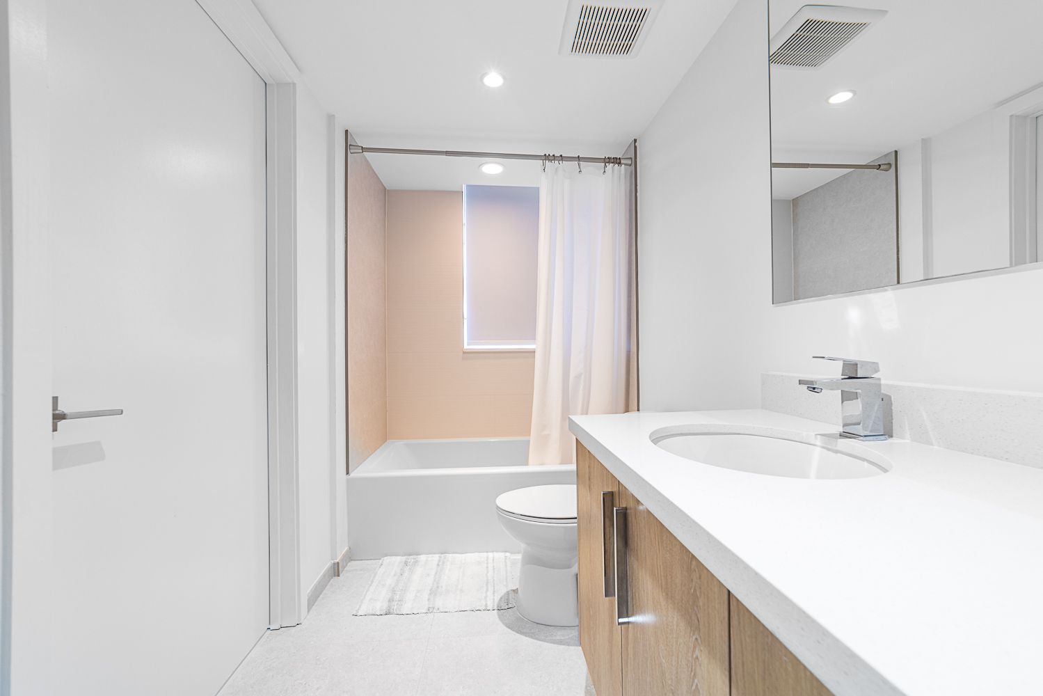 Bright bathroom with white walls, wooden vanity, bathtub, and toilet.