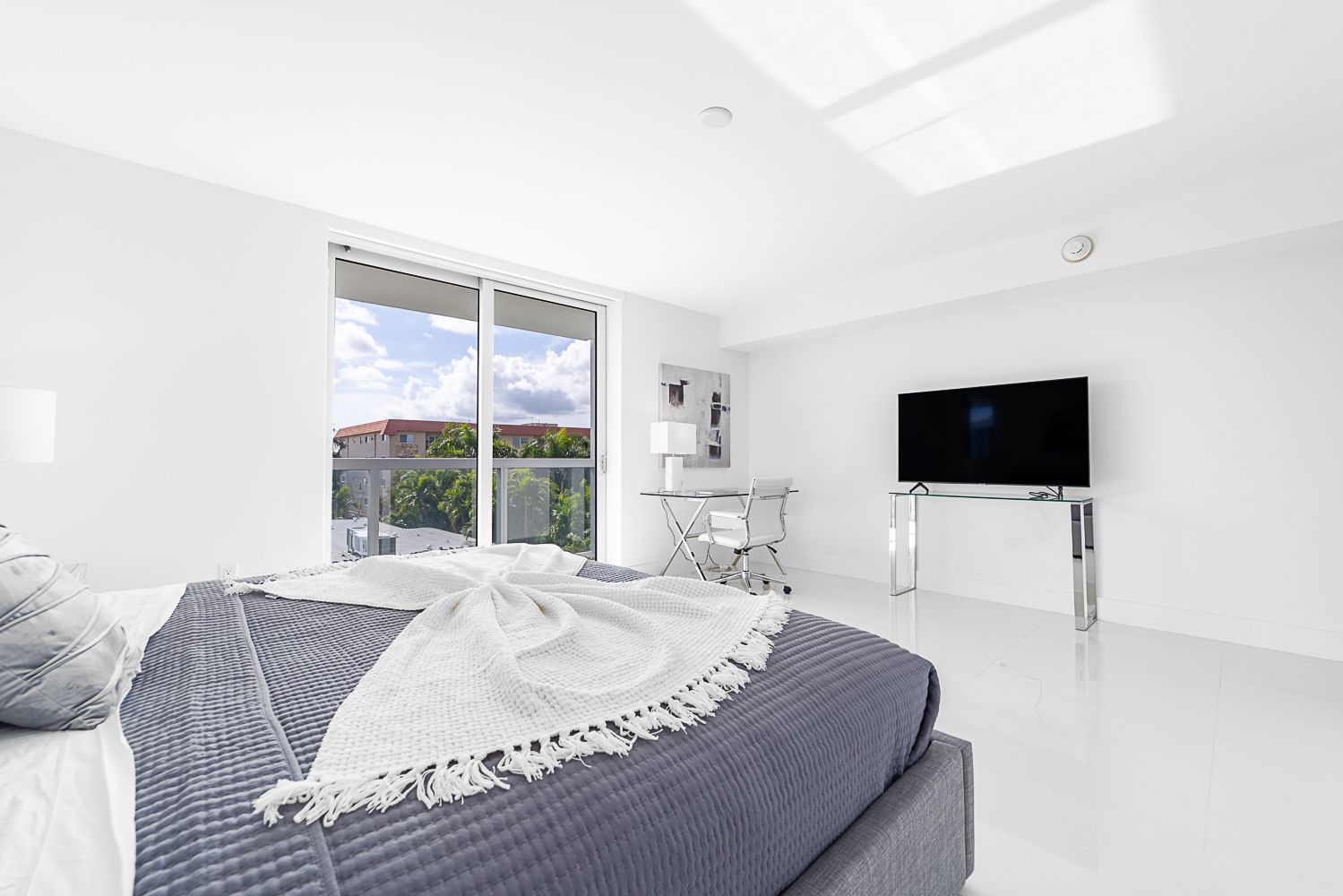 White bedroom with a bed, TV, and balcony view.