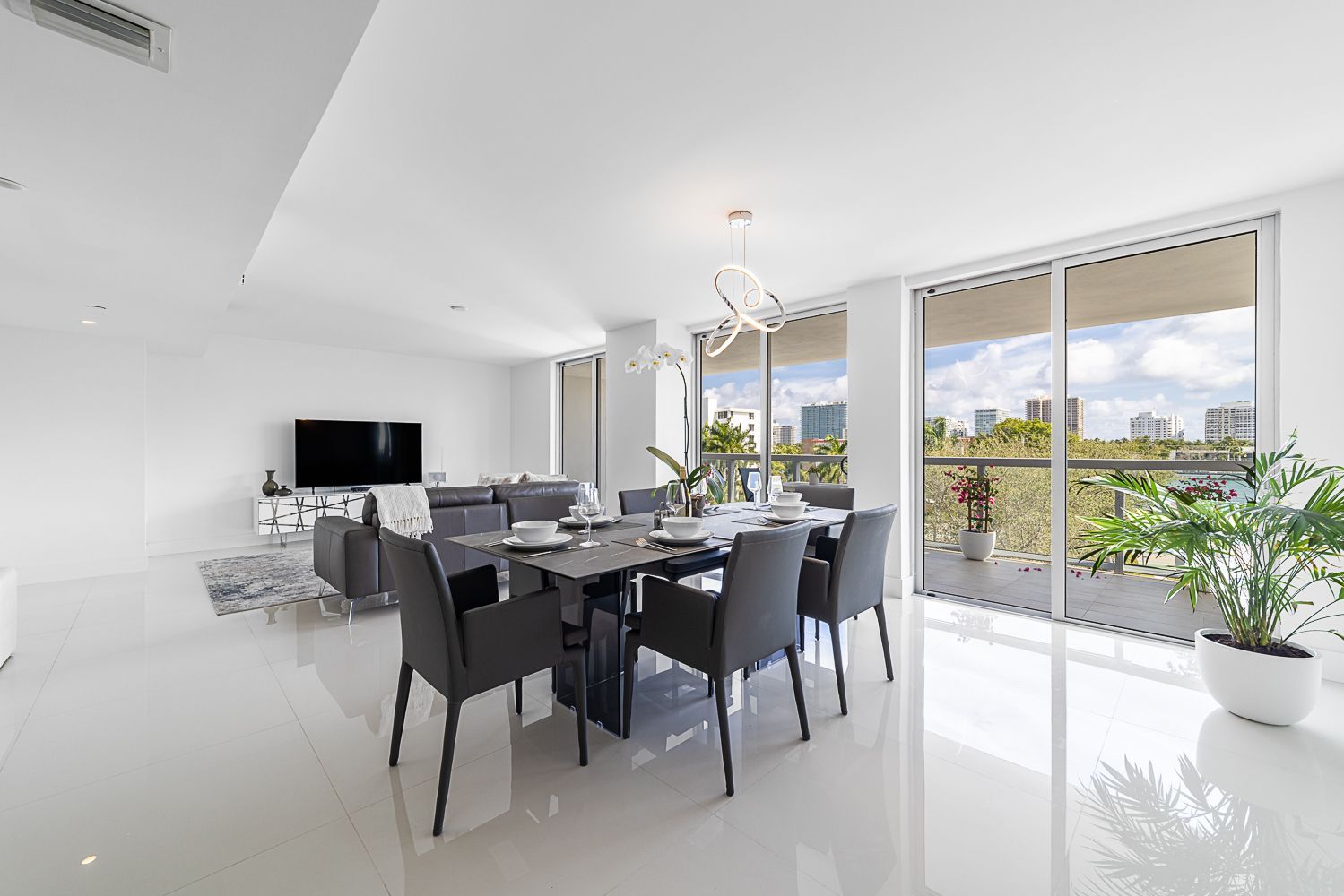 Modern dining room with table and chairs, large windows with a city view, and a potted plant.