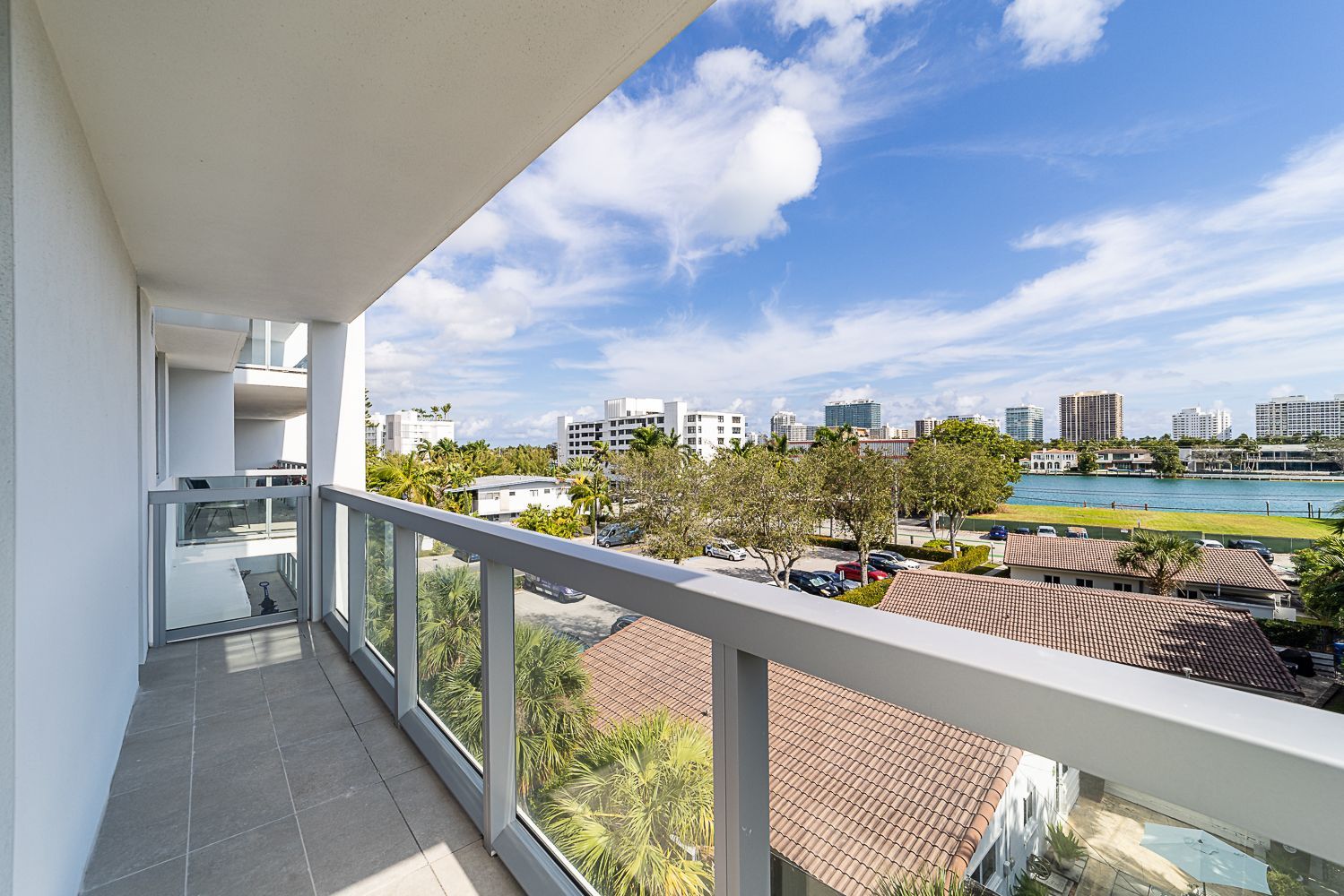 Balcony view: Glass railings, cityscape, blue sky, sunshine.