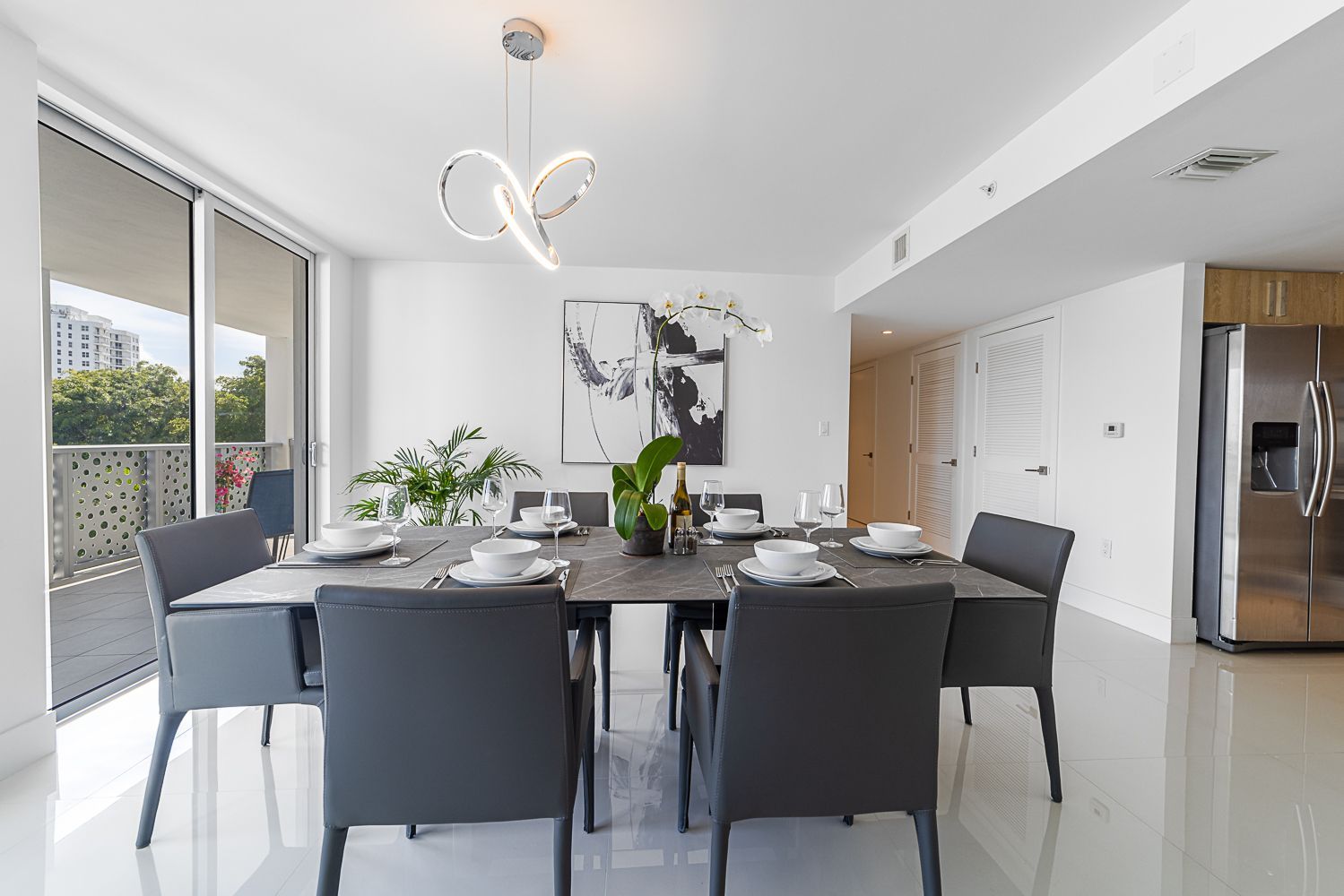 Modern dining room with table set for guests, large windows, and abstract art.