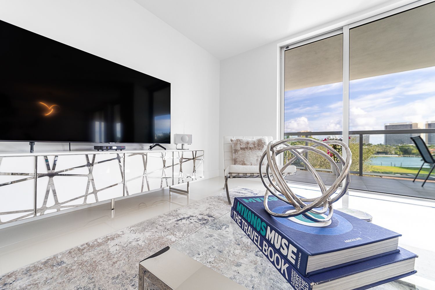 Modern living room with a large TV, white furniture, and balcony view.