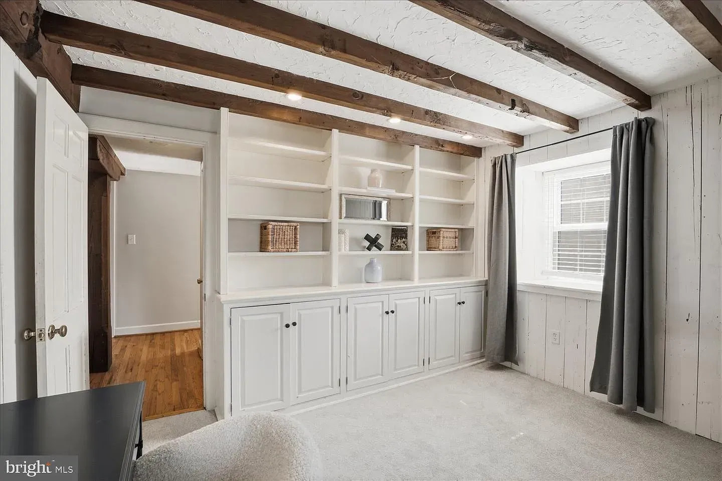 Bright bedroom with exposed ceiling beams, built-in white cabinets, and a window with dark curtains