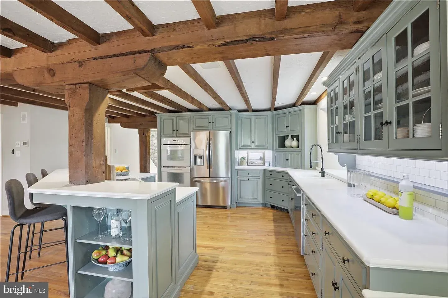 Bright kitchen with wood beams, light blue cabinets, island, and stainless steel refrigerator