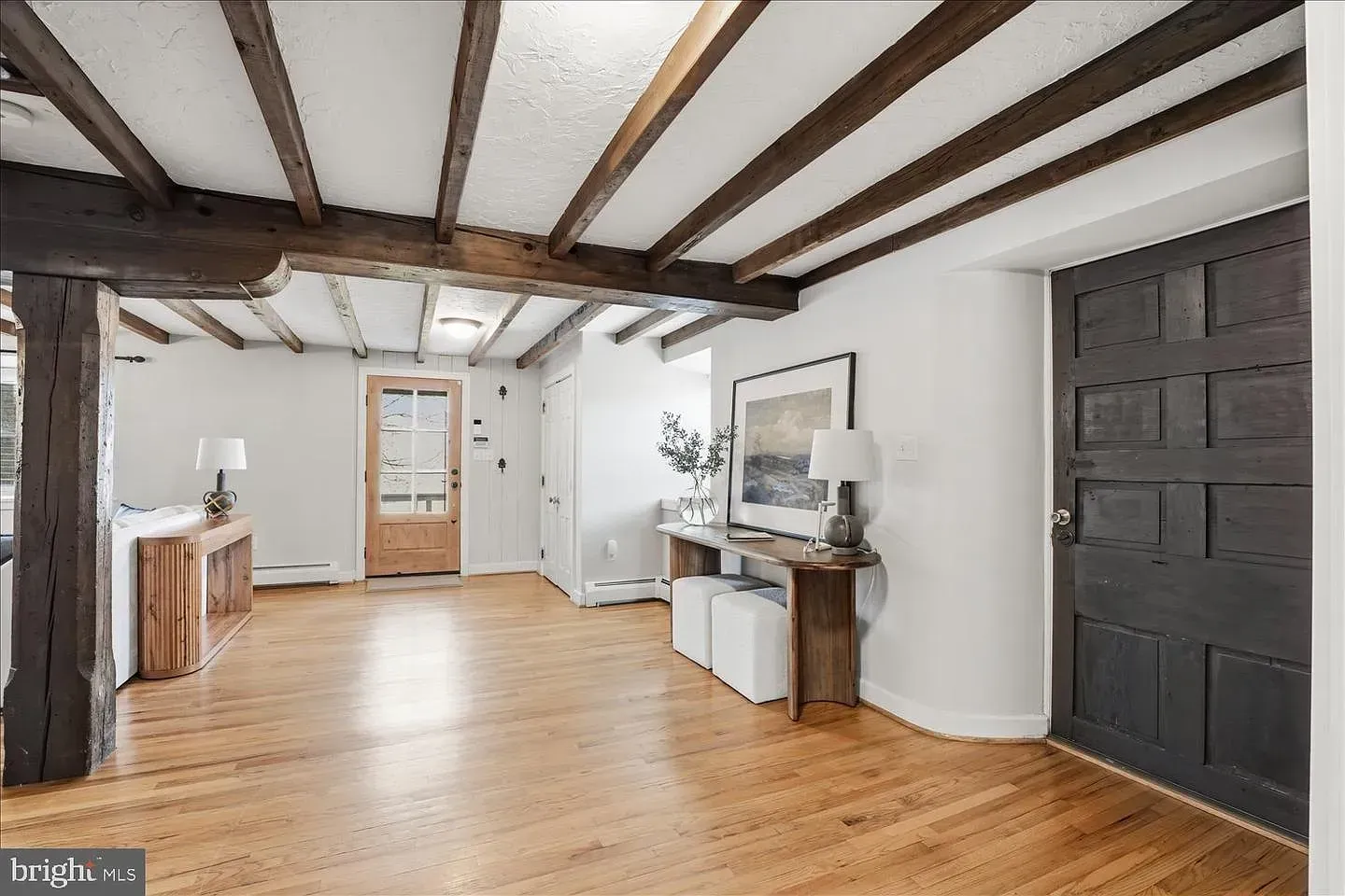 Spacious white room with exposed dark beams, hardwood floors, and a dark door on the right